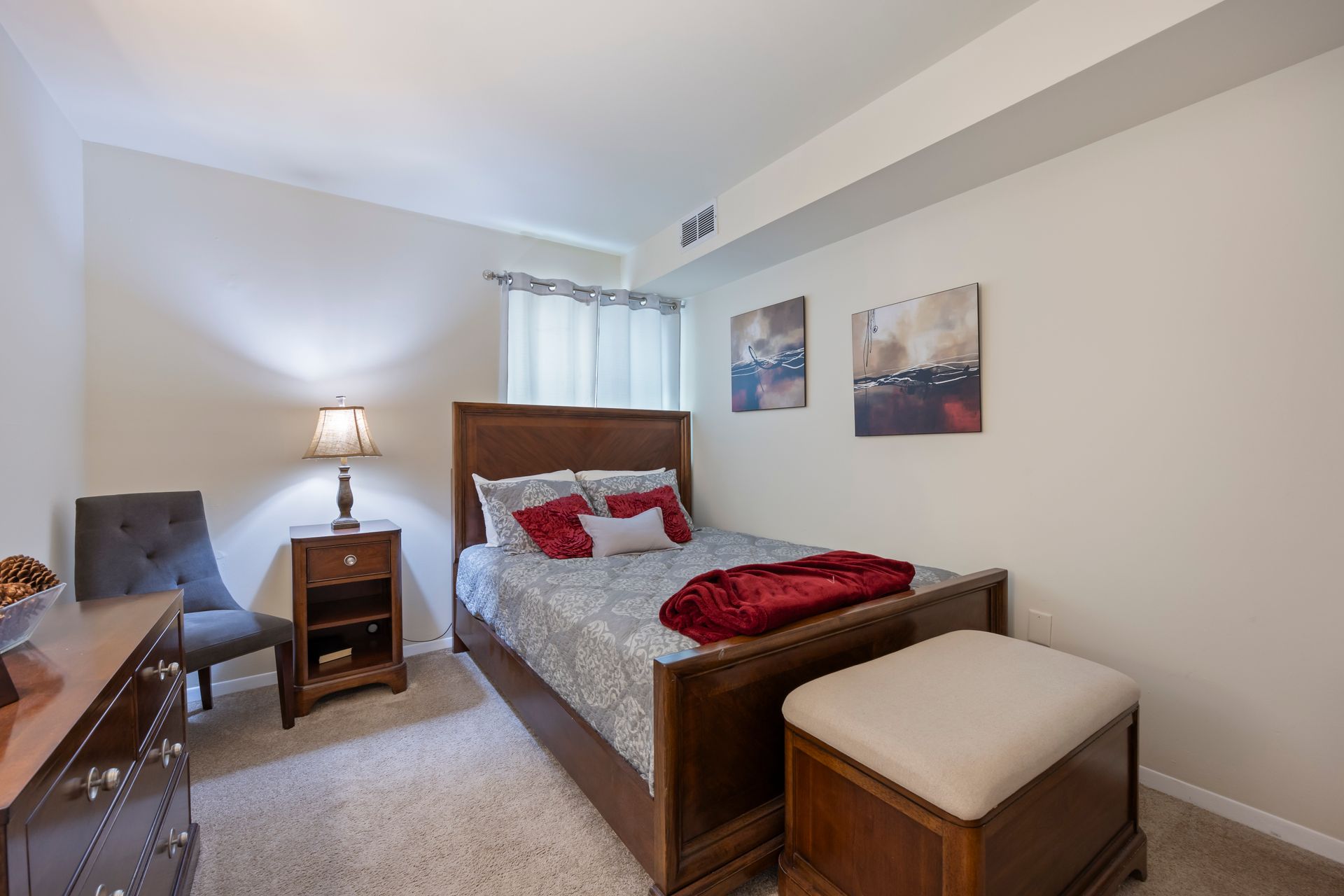 A bedroom with a bed , nightstand , chair and ottoman.