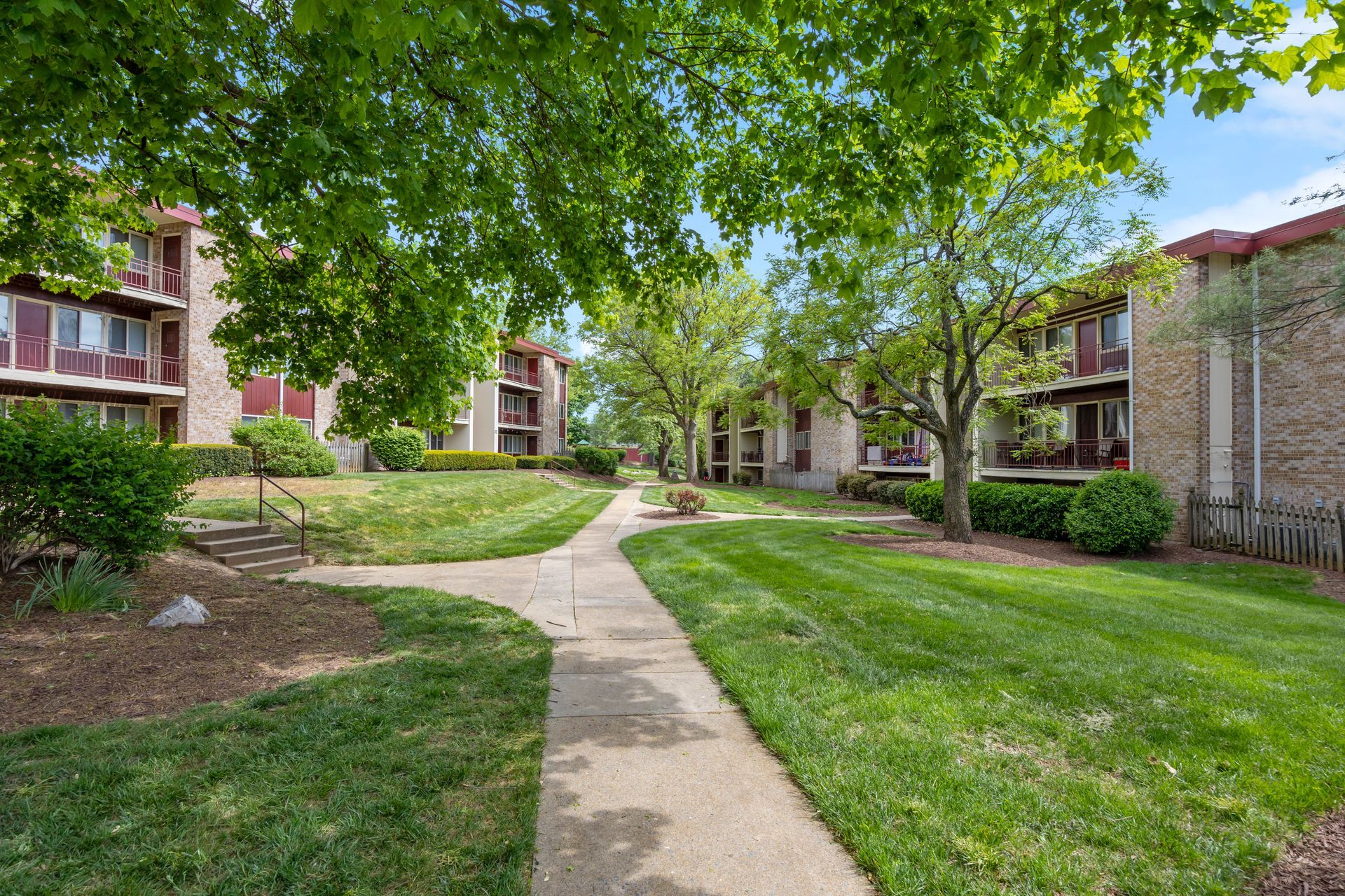 A walkway leading to a row of apartment buildings surrounded by lush green grass.
