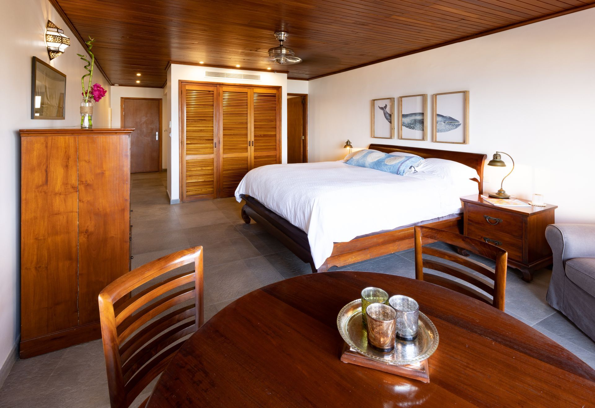 Bedroom with wooden furniture, bed, table, and storage cabinets. Brown and white tones.