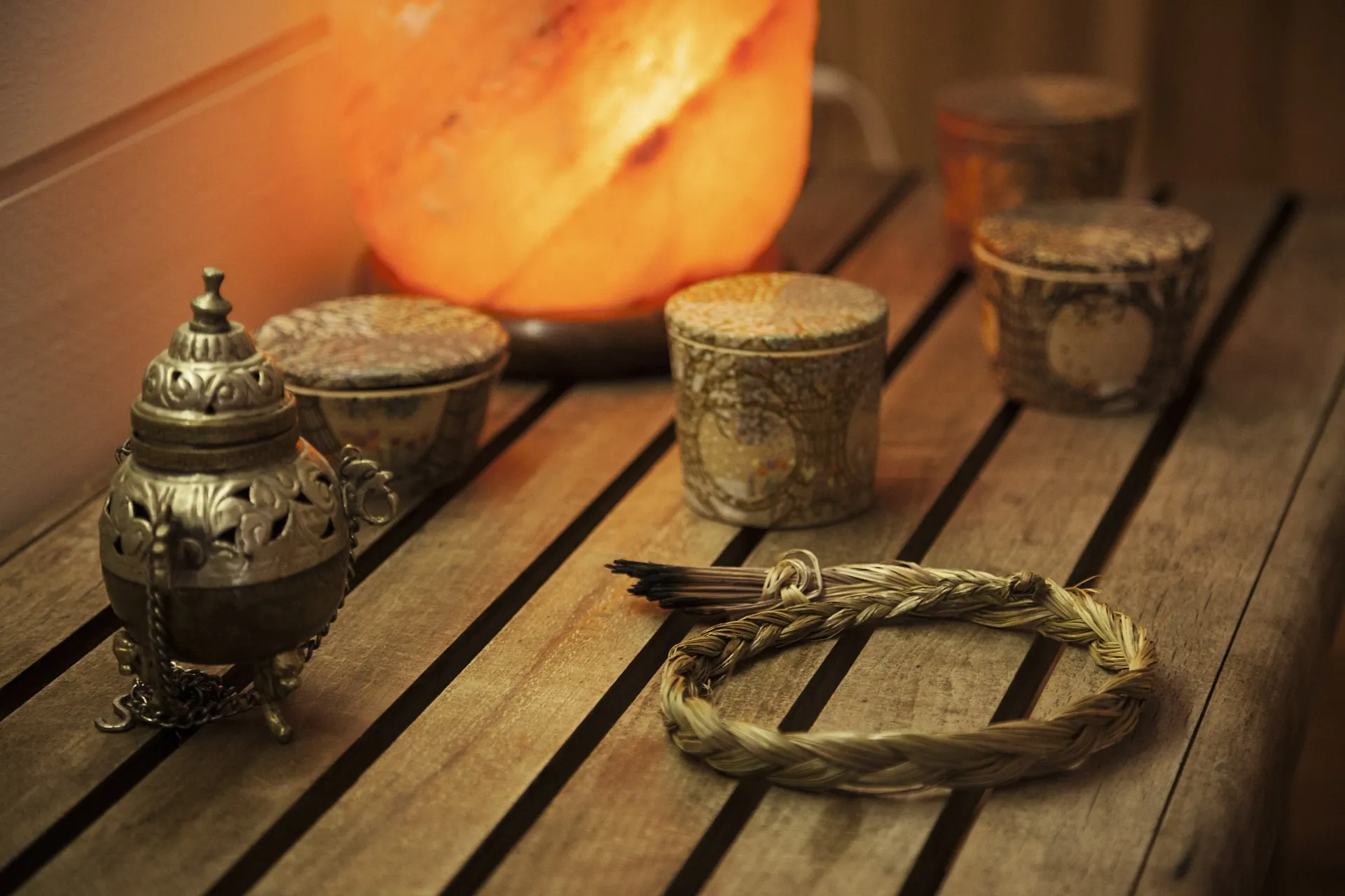 A warm, dim scene on a wooden surface with a glowing Himalayan salt lamp and various decorative containers.