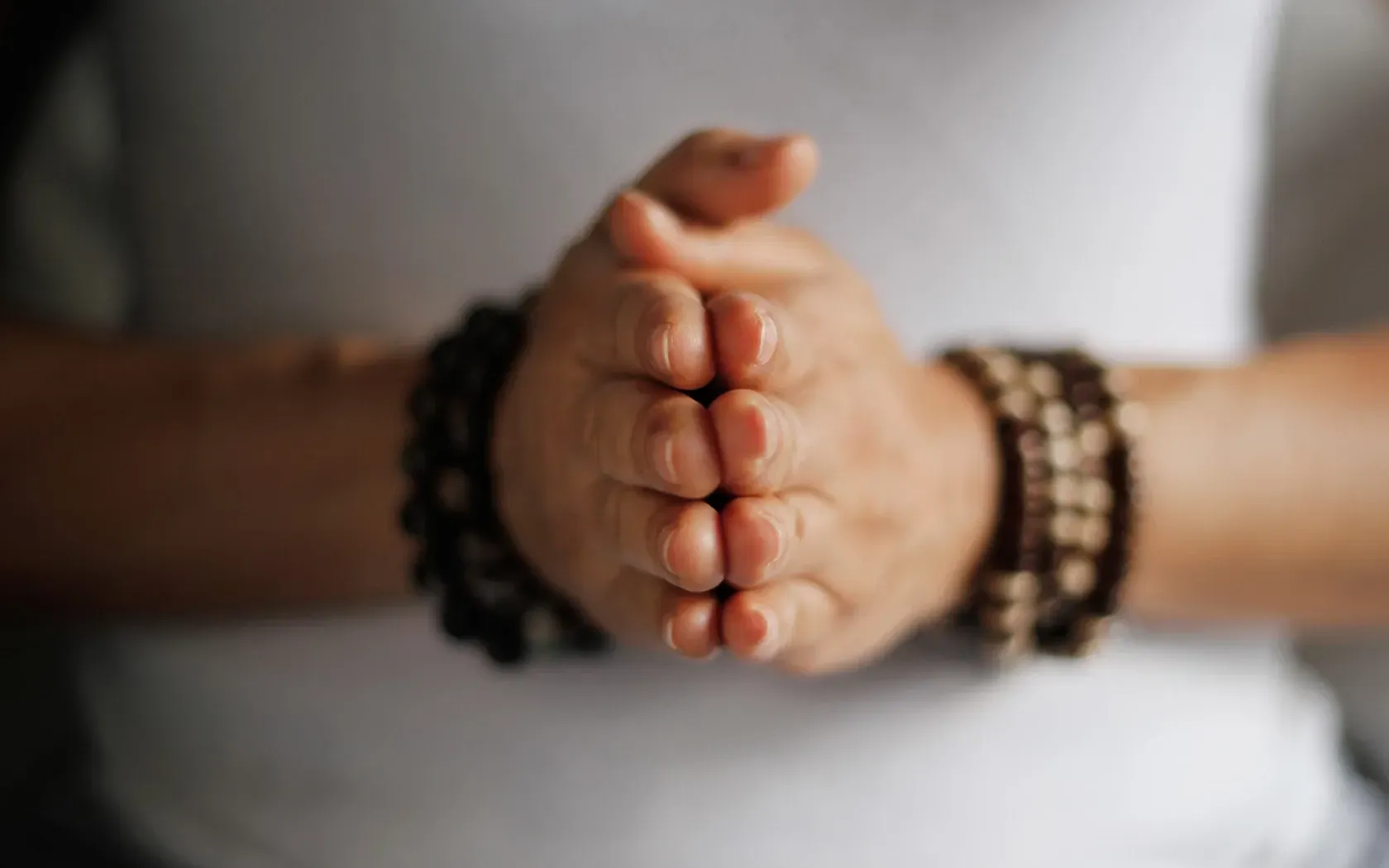 Hands clasped together in prayer, wearing beaded bracelets.