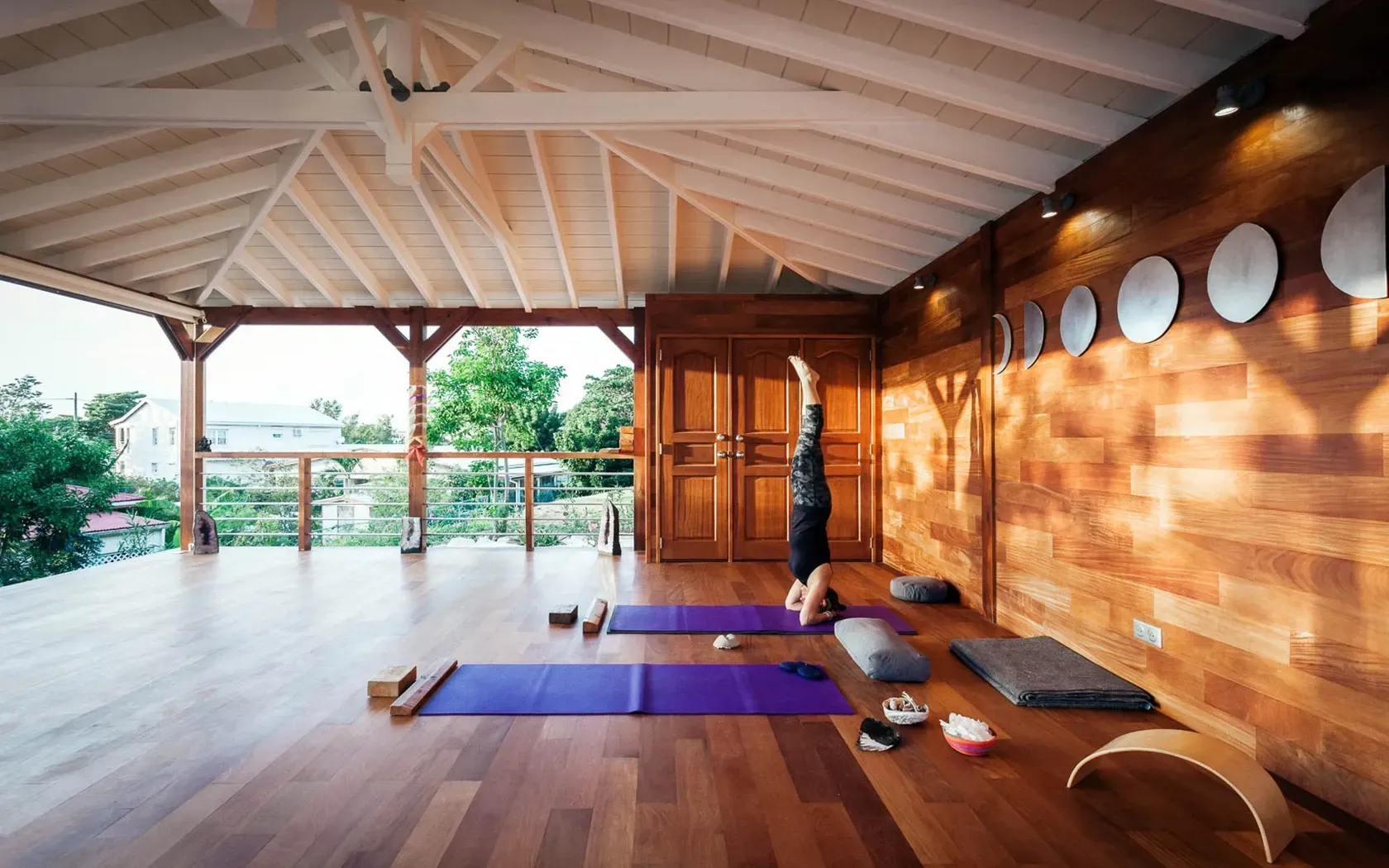 Yoga studio with a person in a headstand. Wooden floors, mats, and natural light.
