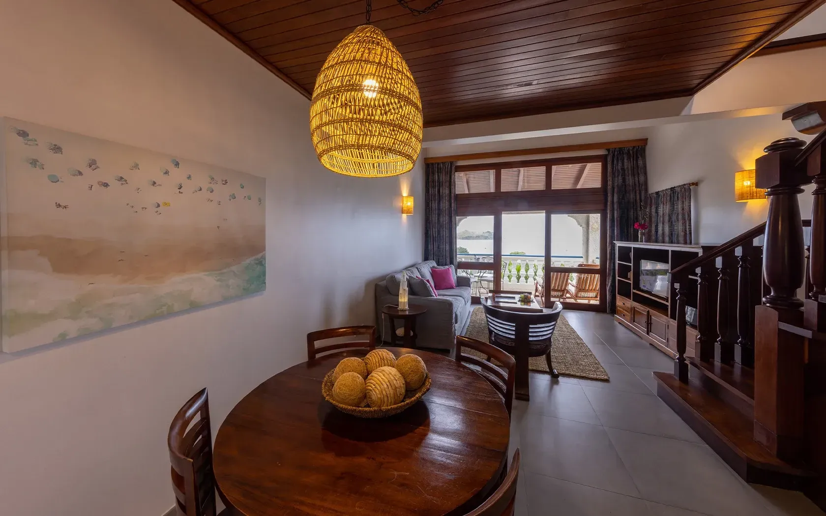 Dining area of a coastal apartment with a wooden table, chairs, and a hanging light.
