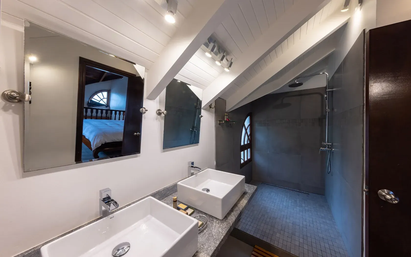 Bathroom with white sinks, mirrors, gray shower, and dark brown door.