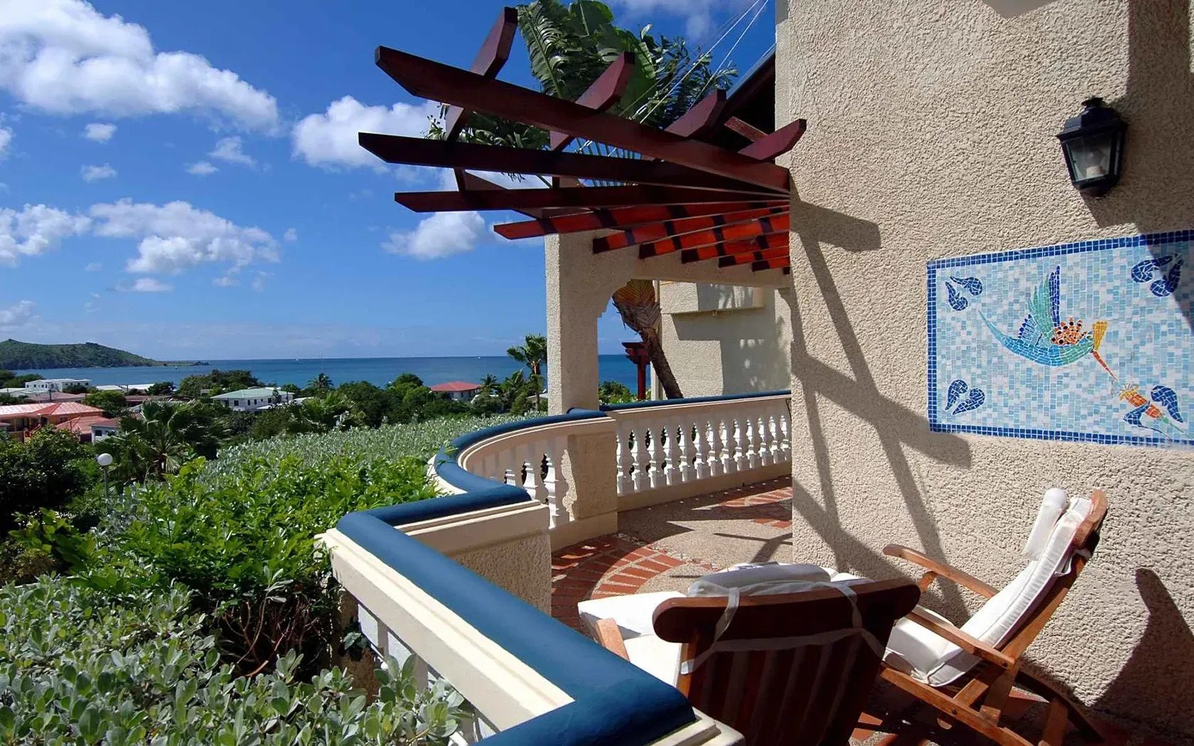 Balcony overlooking ocean with wooden pergola and mosaic art.