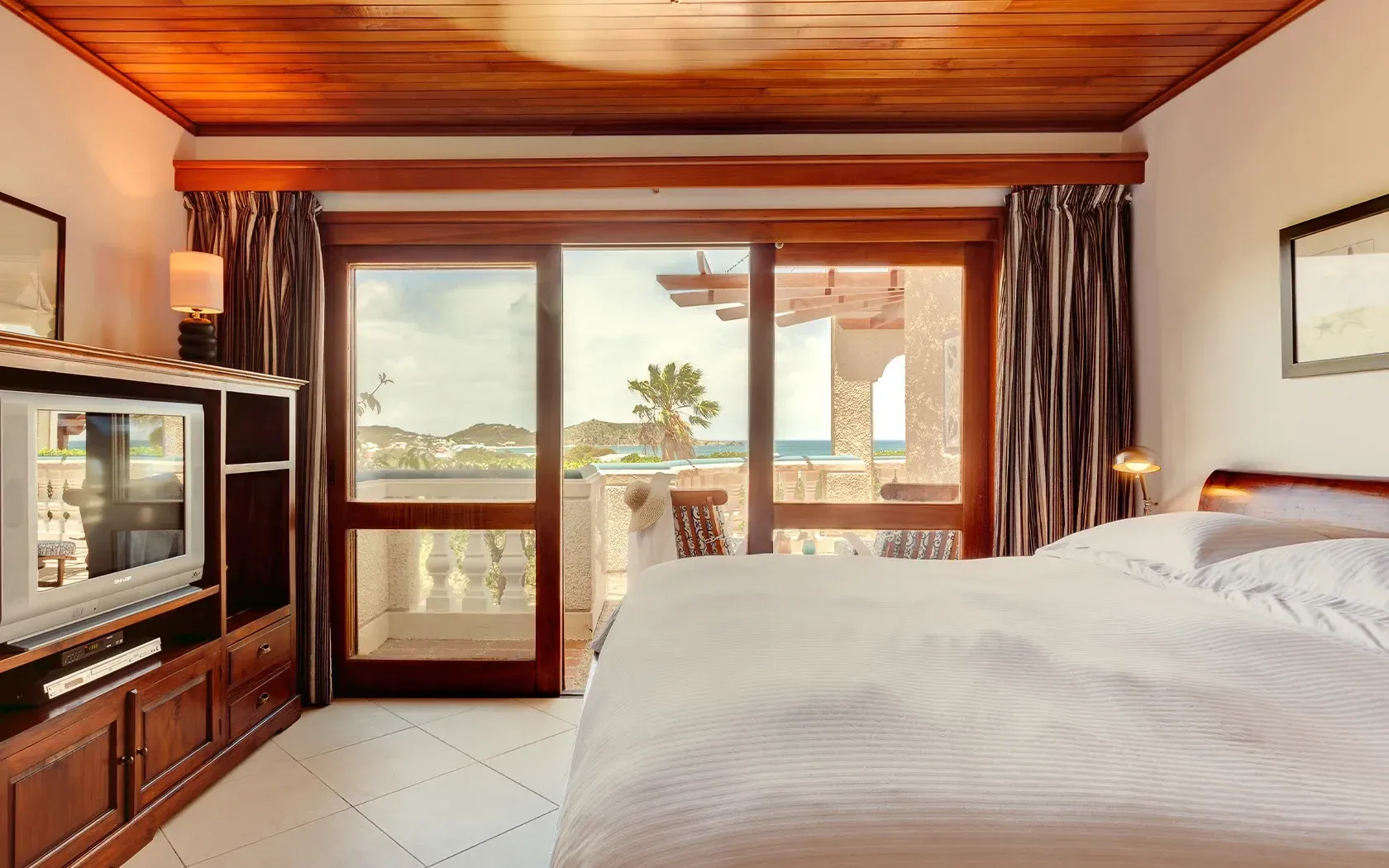 Bedroom with ocean view, large bed, sliding glass door, wooden TV cabinet, and wood ceiling.