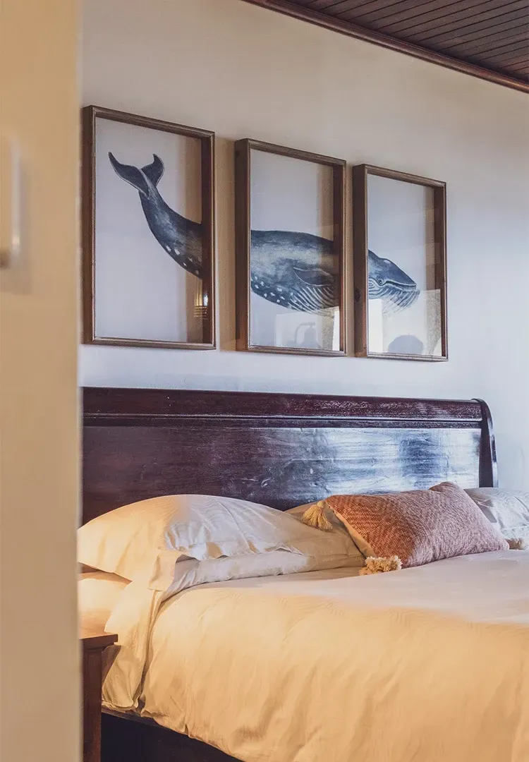 Bedroom with whale art above a bed, featuring white linens, and a dark wood headboard.