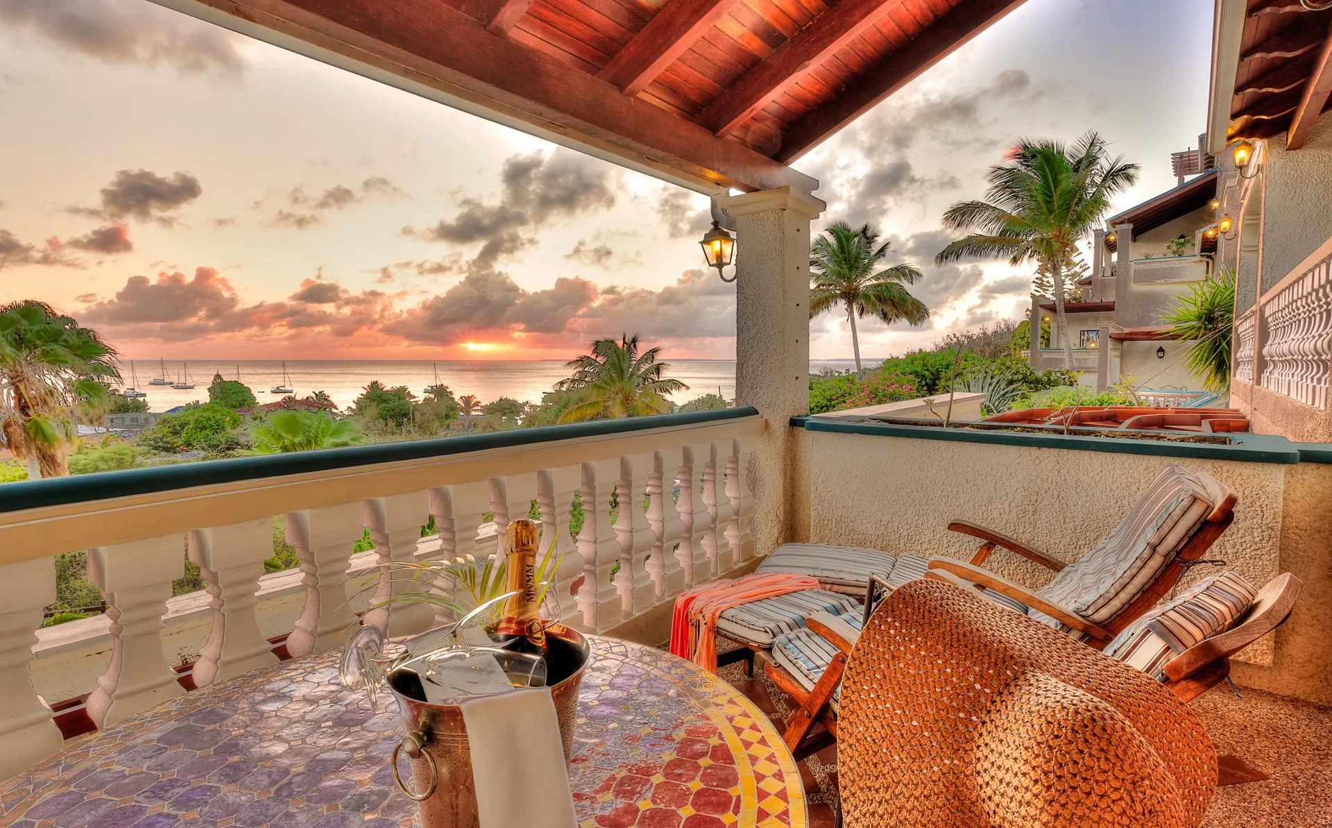 Balcony overlooking ocean at sunset, with table, chairs, and champagne.
