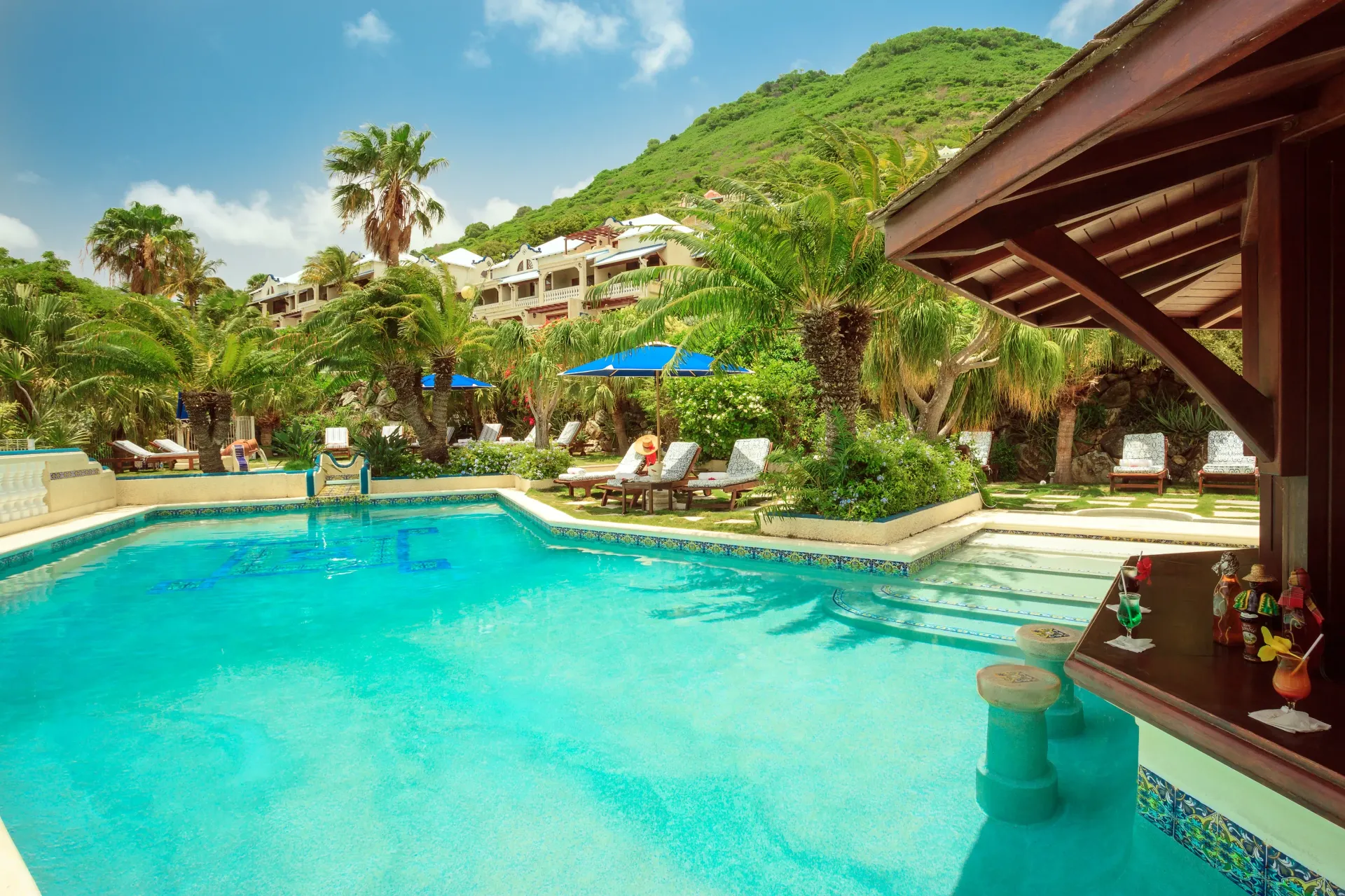Swimming pool with swim-up bar in a tropical resort setting. Lush green foliage and mountain backdrop.