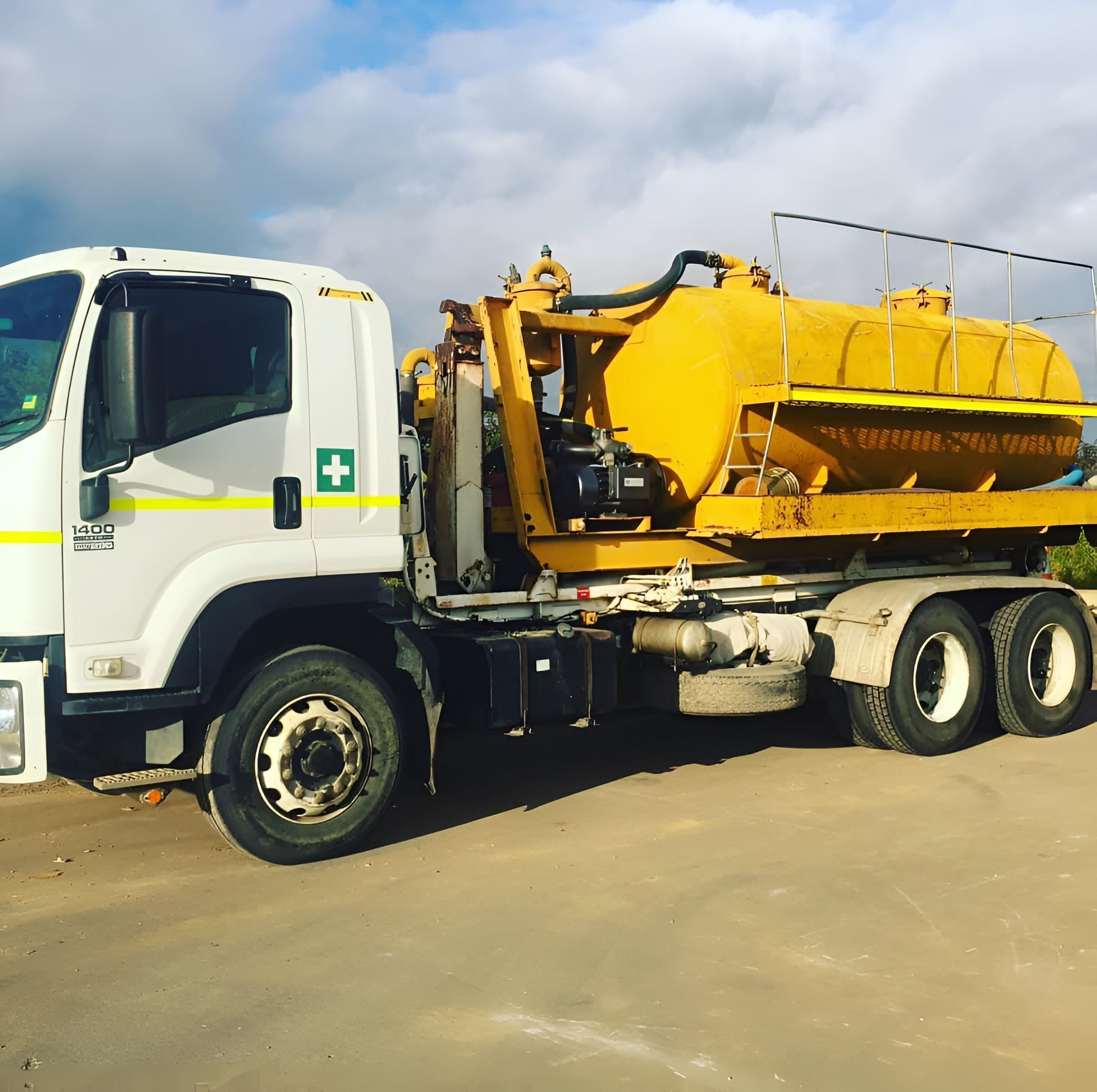 Yellow septic tank truck, white cab, on a paved surface, under a cloudy sky.