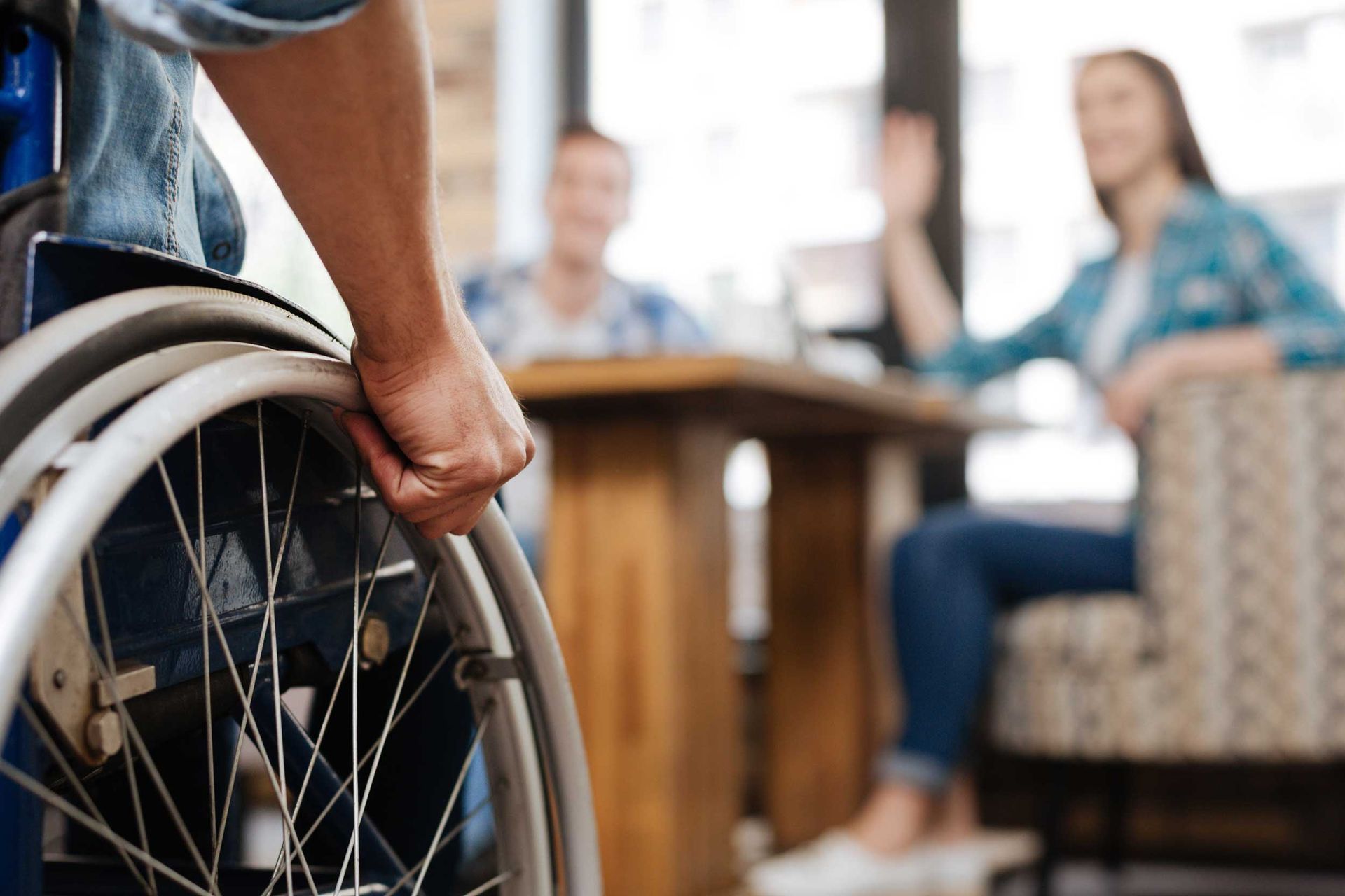 Person holding a wheelchair in a living room with two people seated in the background