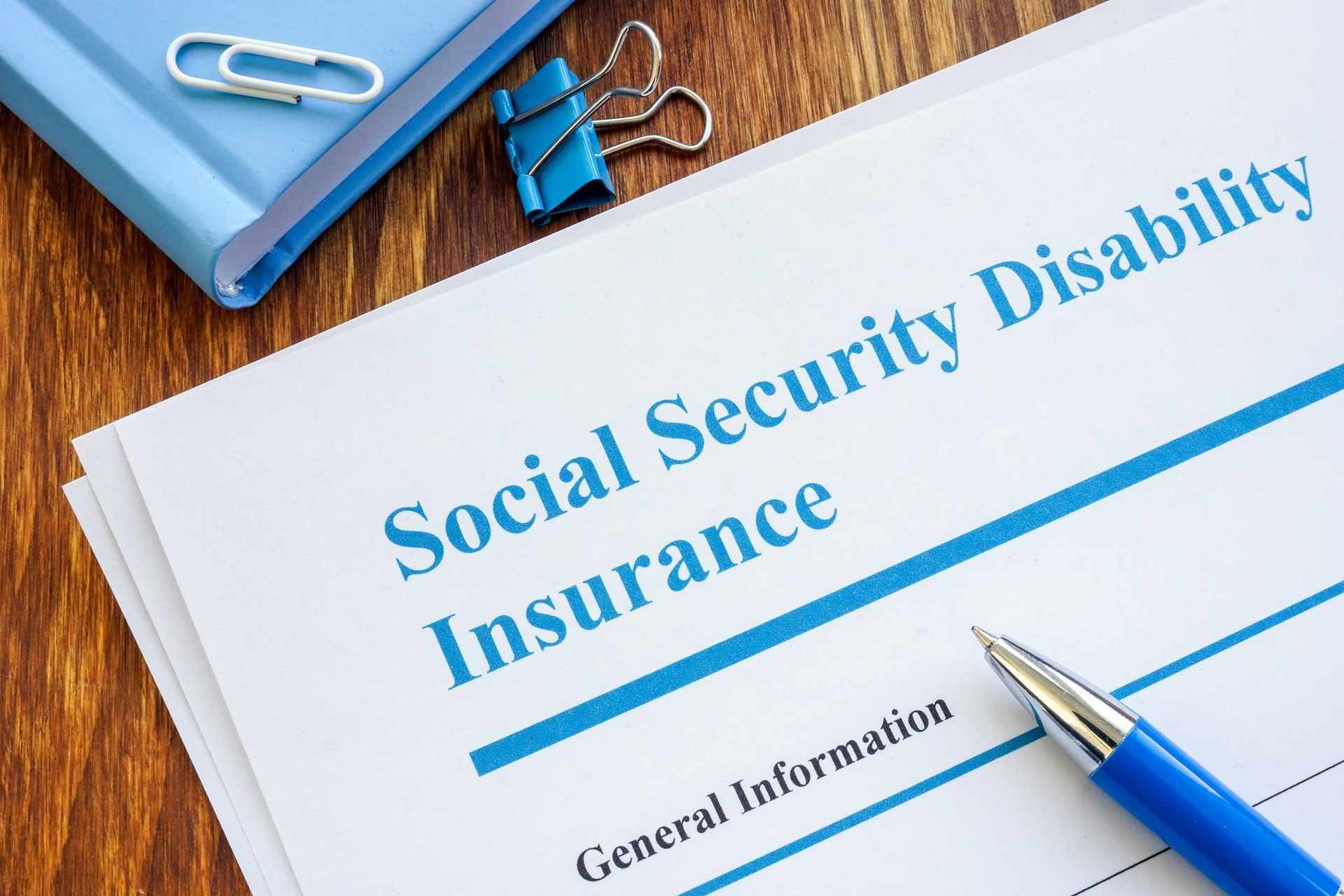Social Security Disability Insurance form on desk with blue pen and binder clip Social Security Disability Insurance form on desk with blue pen and binder clip