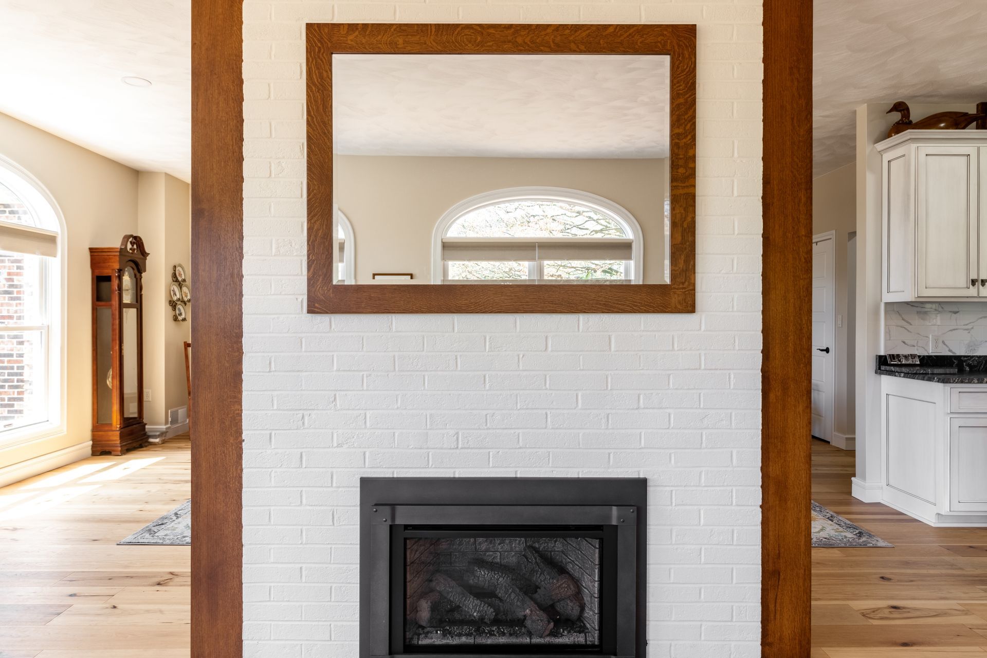 Fireplace with white brick surround, brown wood beams, and large mirror.
