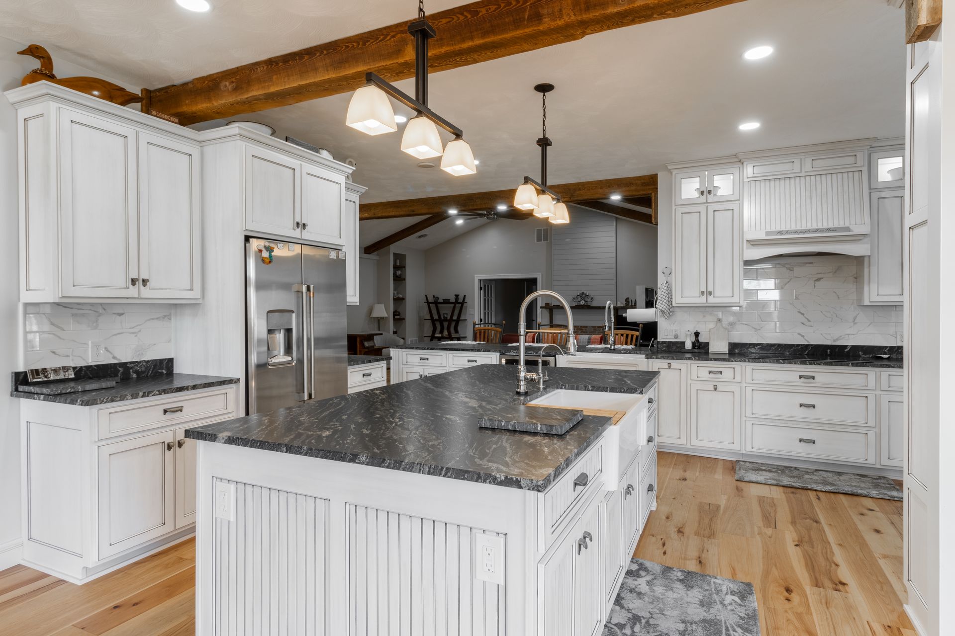 White kitchen with granite countertops, wooden beams, and stainless steel appliances.