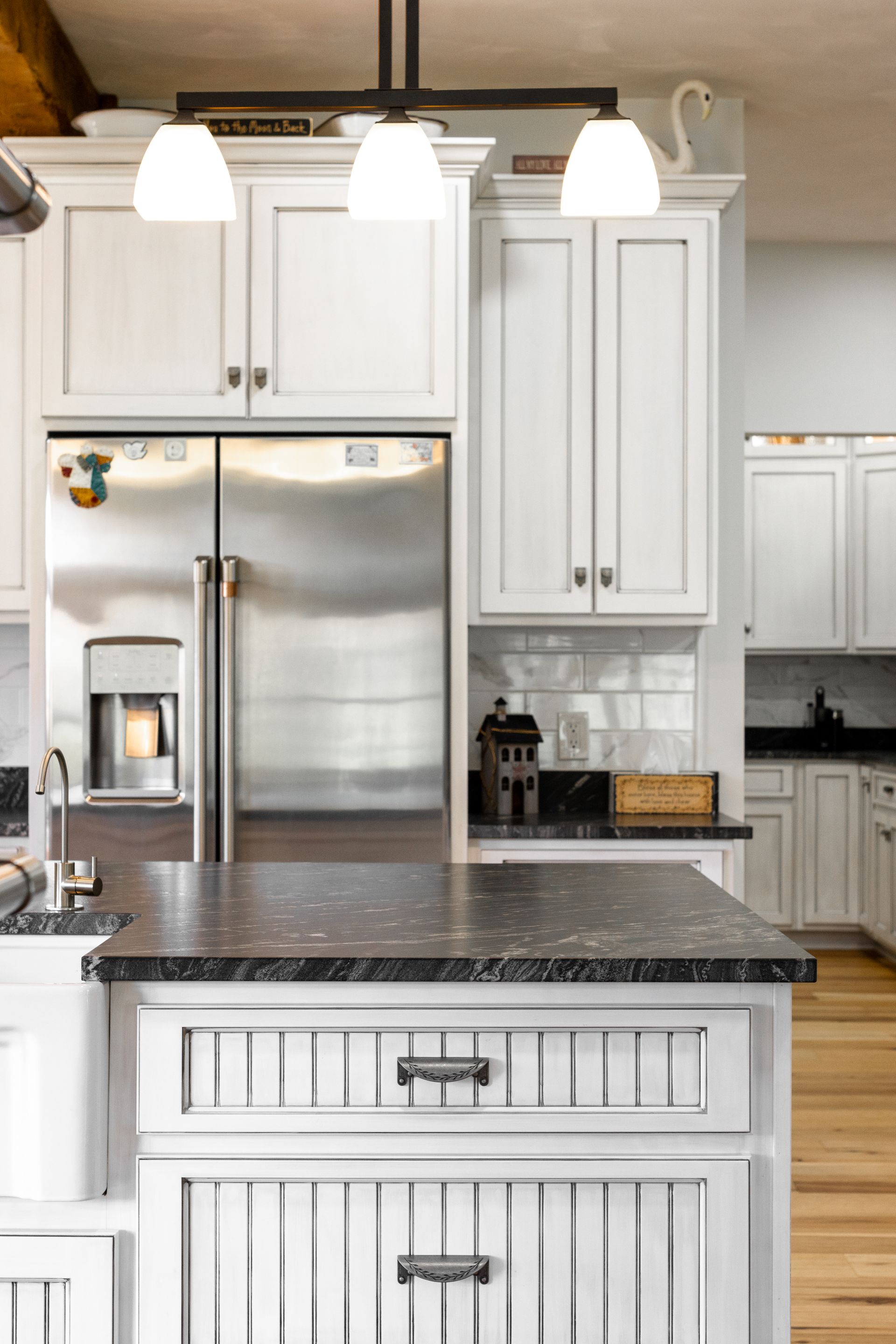 White kitchen with stainless steel fridge, dark countertop island, and hanging lights.