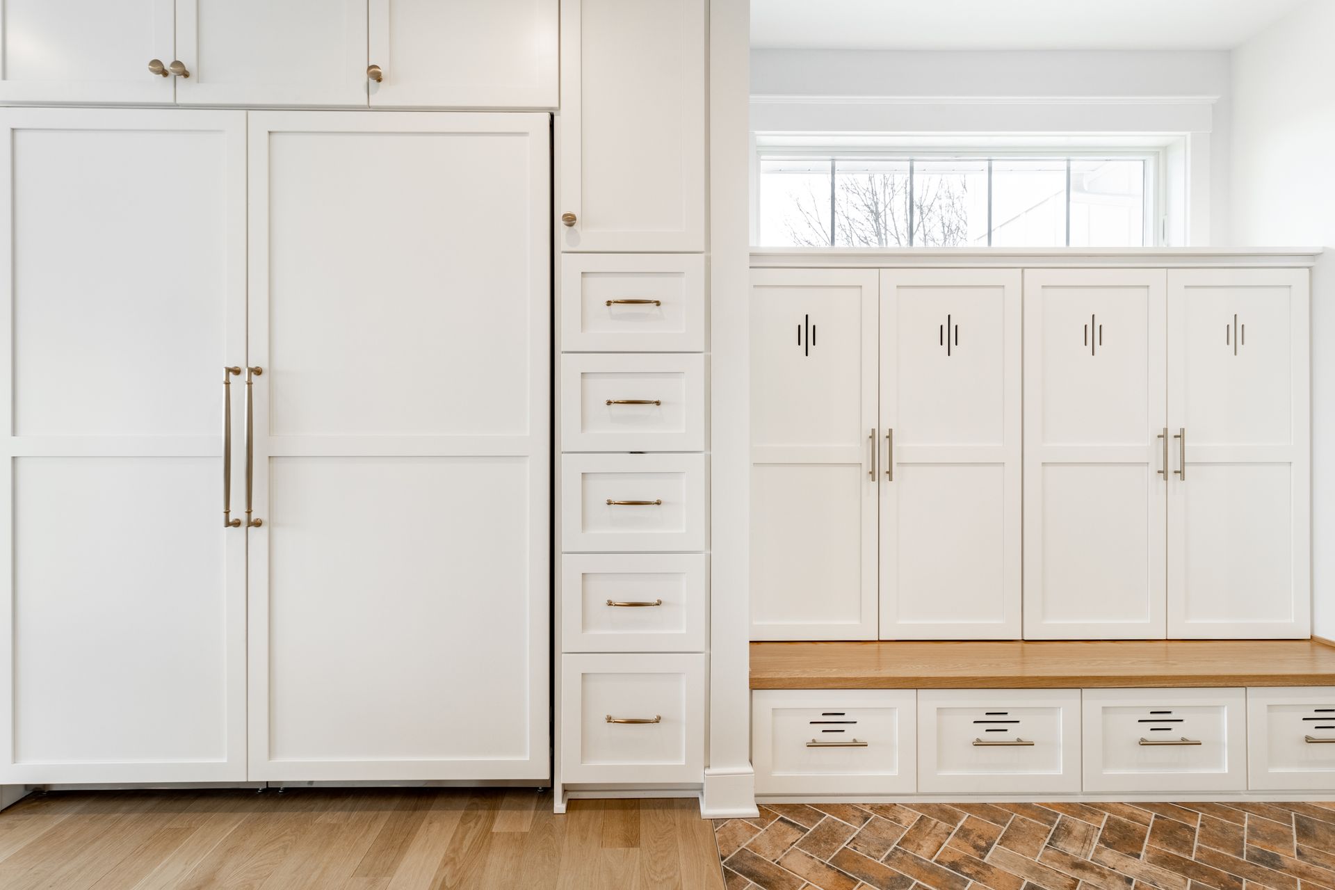 White kitchen cabinets with built-in refrigerator, drawers, and lockers, with wooden floors and window.