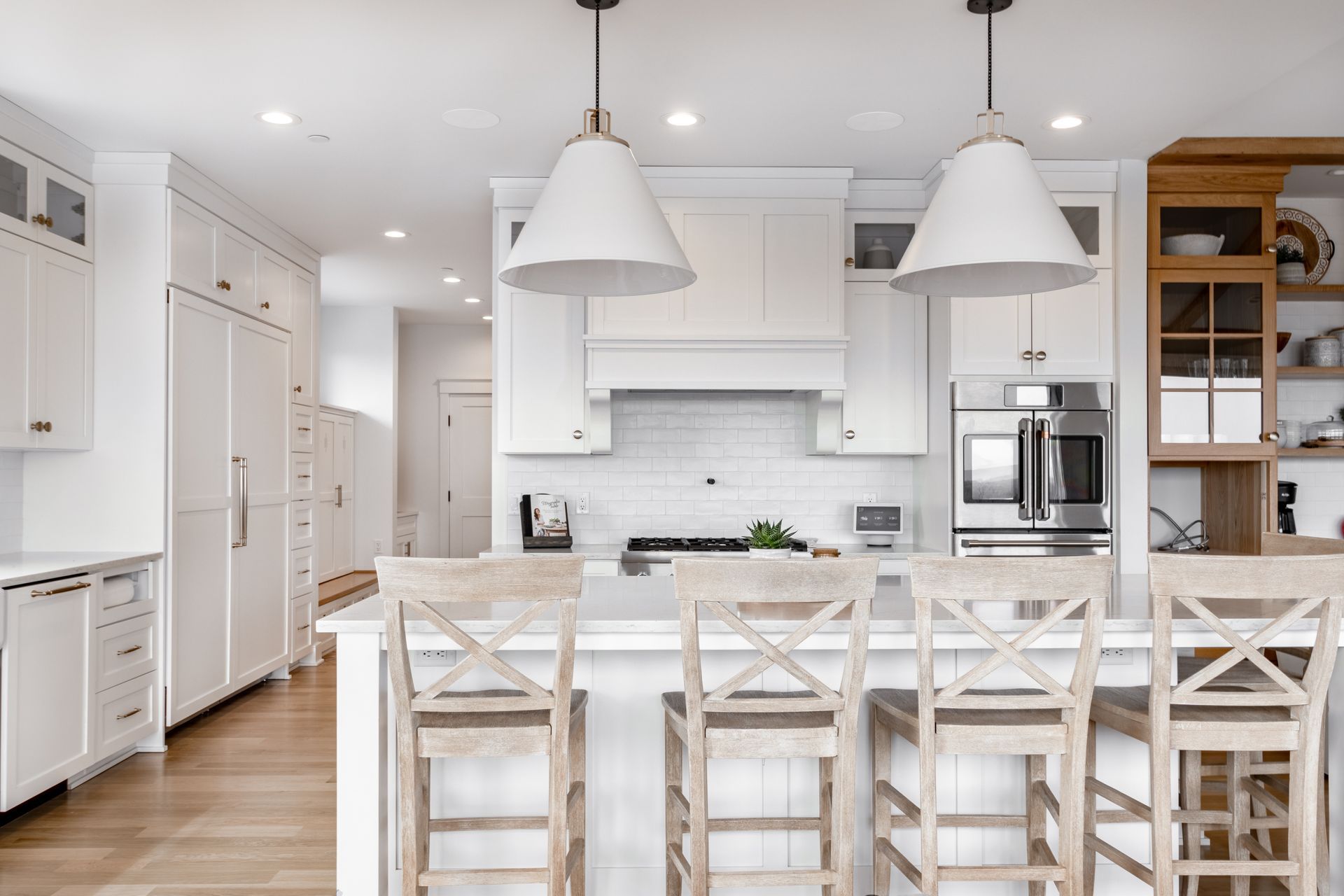 White kitchen with island and light wood stools, pendant lights, and stainless steel appliances.