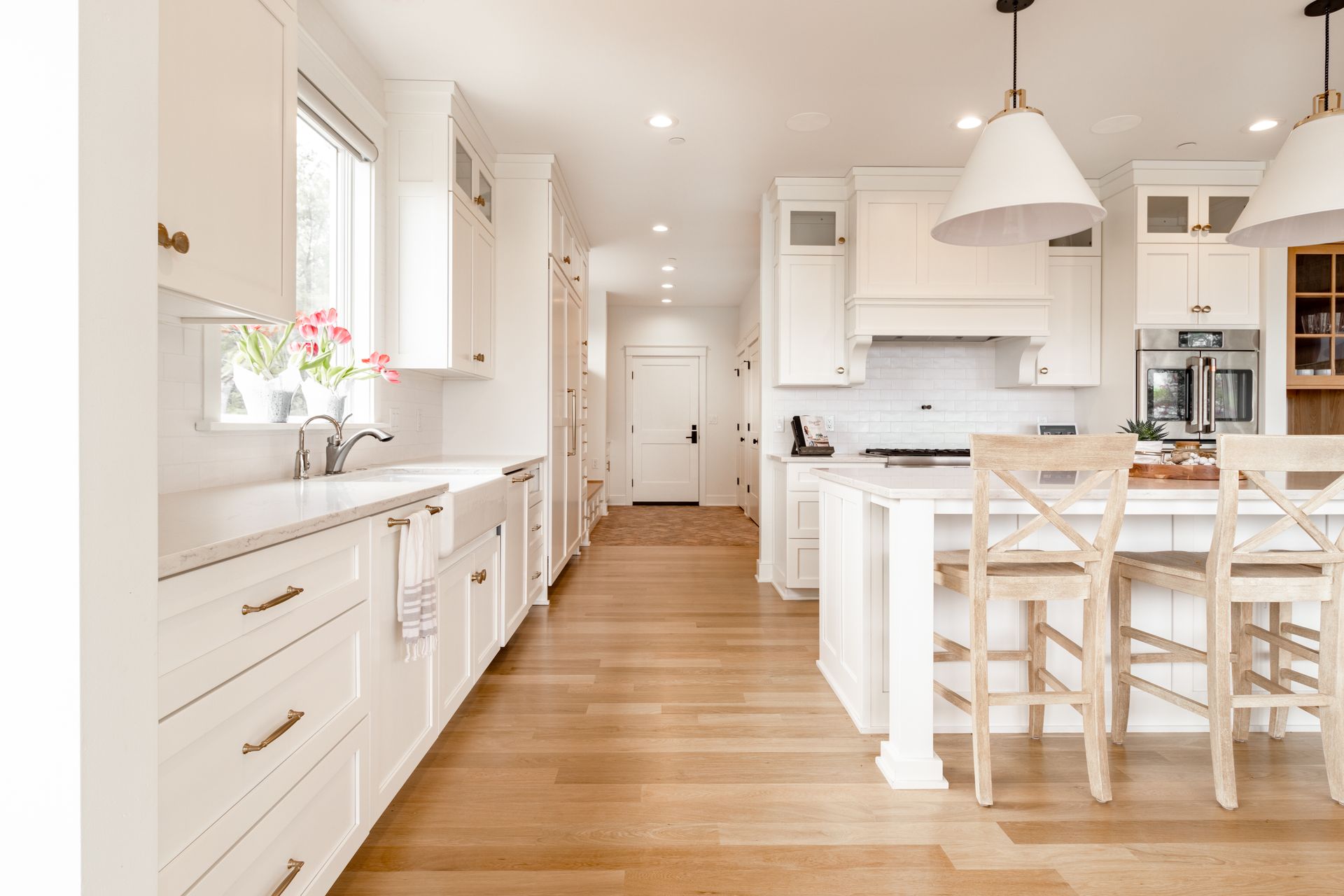 Bright white kitchen with wooden floors, island, and overhead lights.