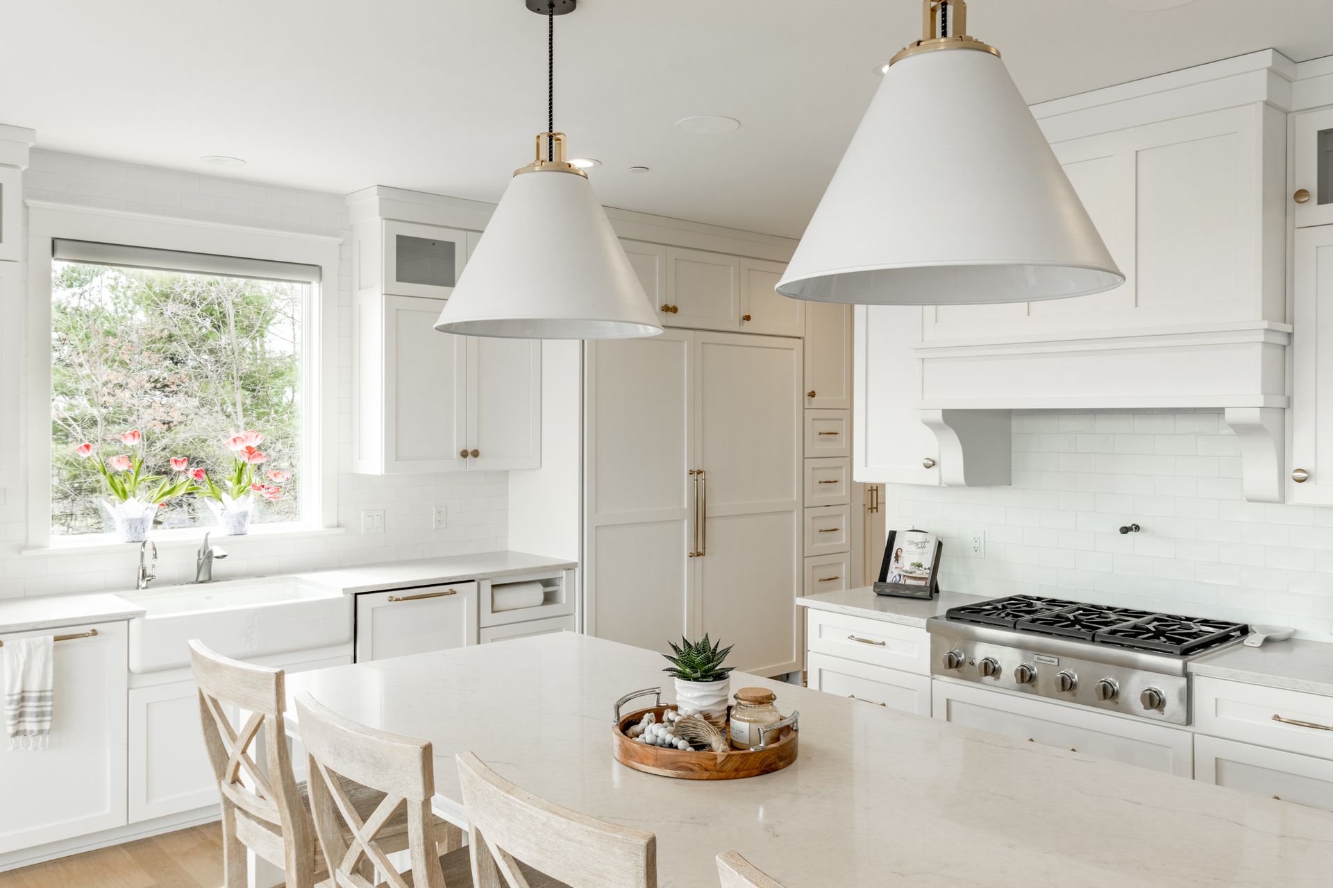 White kitchen with island, pendant lights, gas range, and window overlooking greenery.