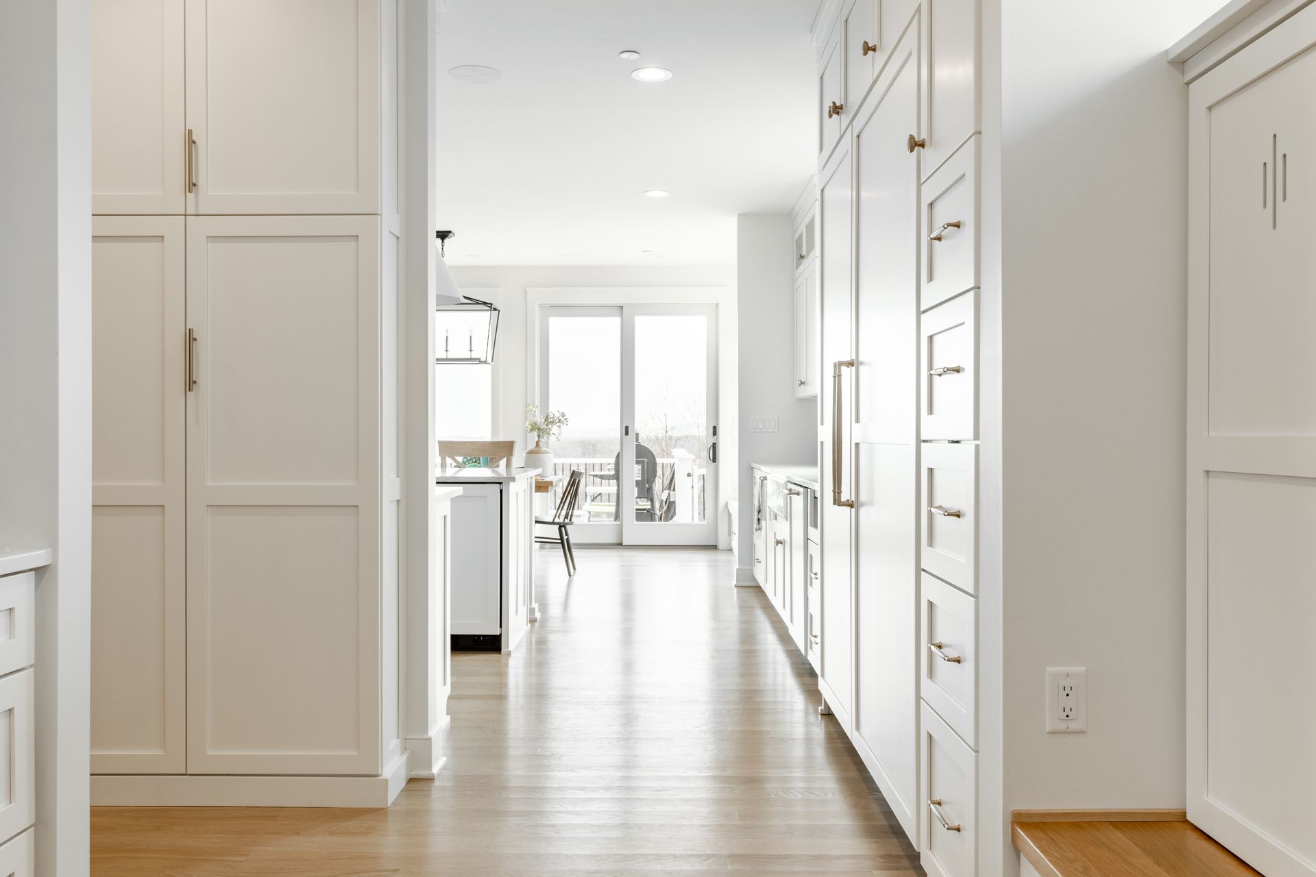 Hallway with white cabinets and hardwood floors leading to a kitchen with a sliding door.