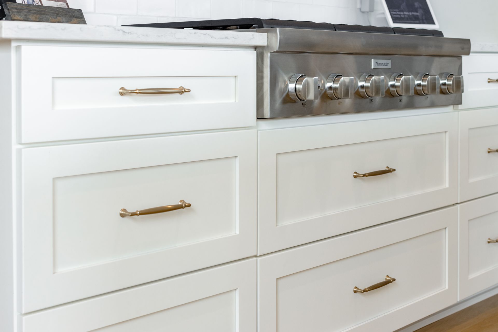 White kitchen cabinets with brass handles under a stainless steel range.