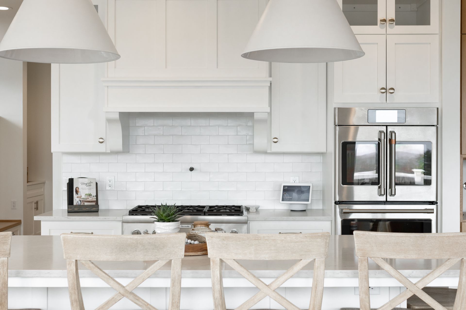 White kitchen with island seating, stainless steel appliances, and two pendant lights.