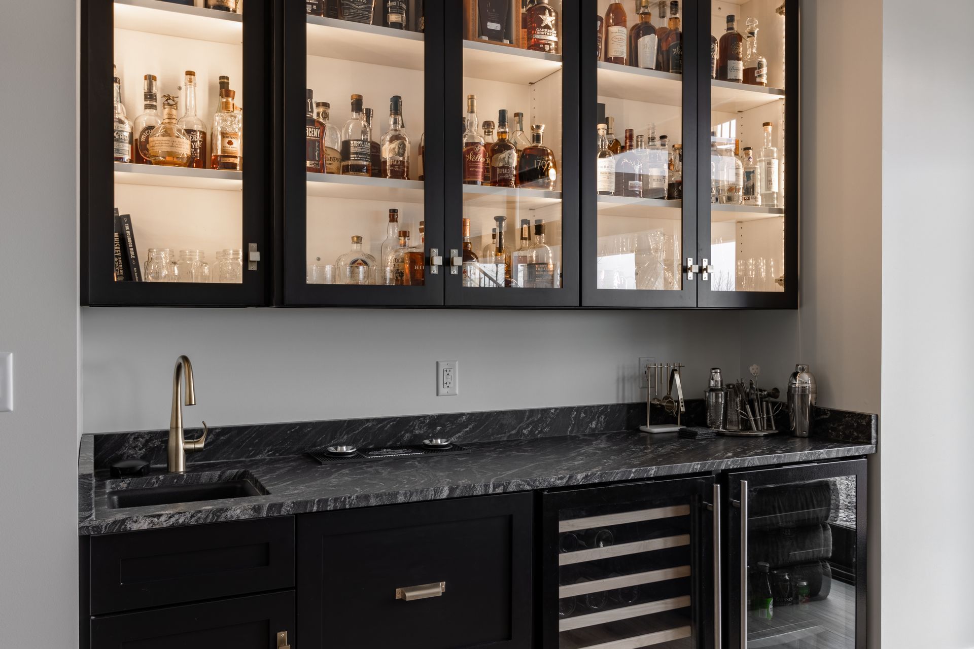 Black home bar with glass-front cabinets, countertop, sink, and two built-in refrigerators.