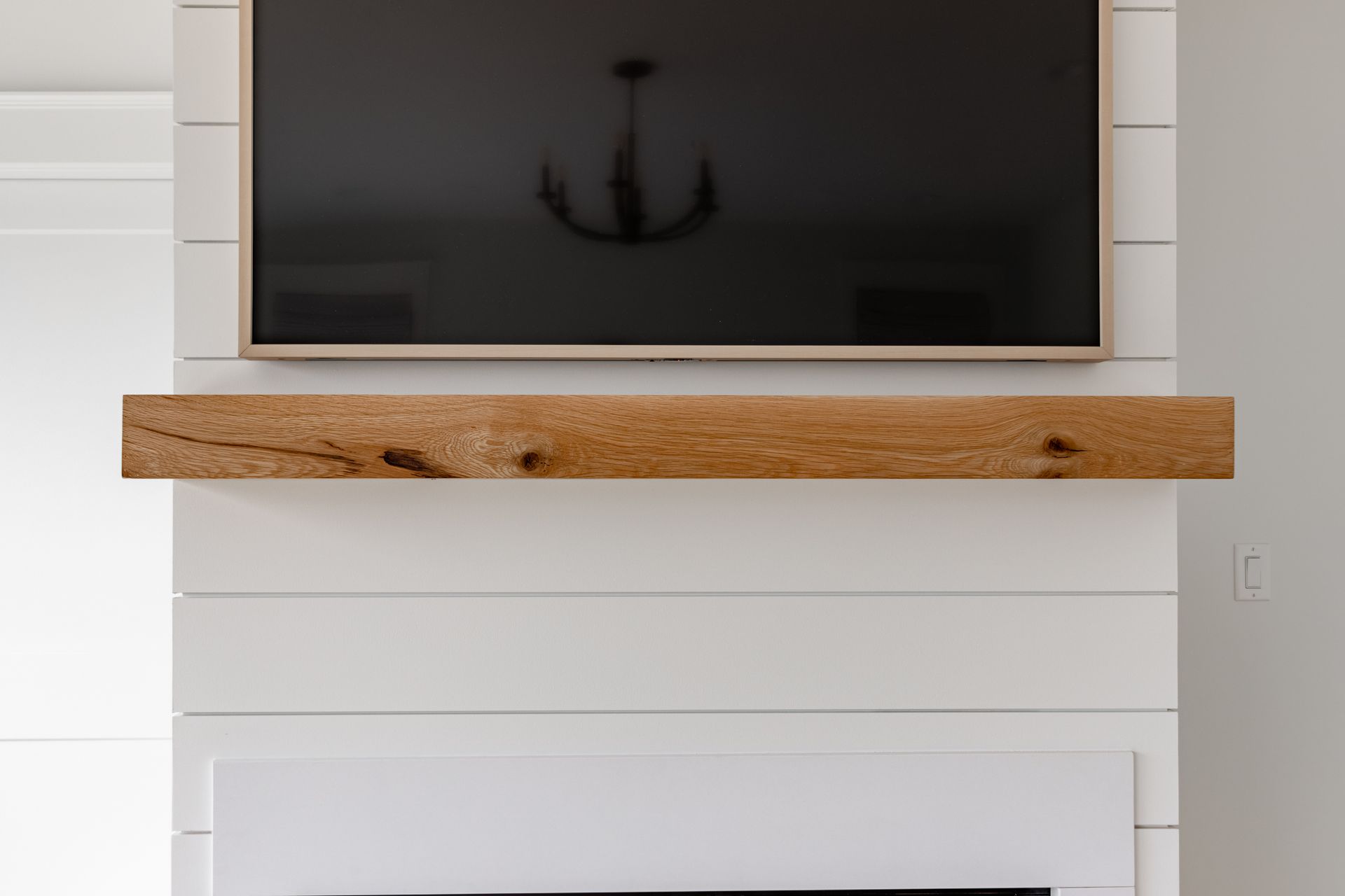 Wooden beam shelf under a mounted TV against a white shiplap wall.