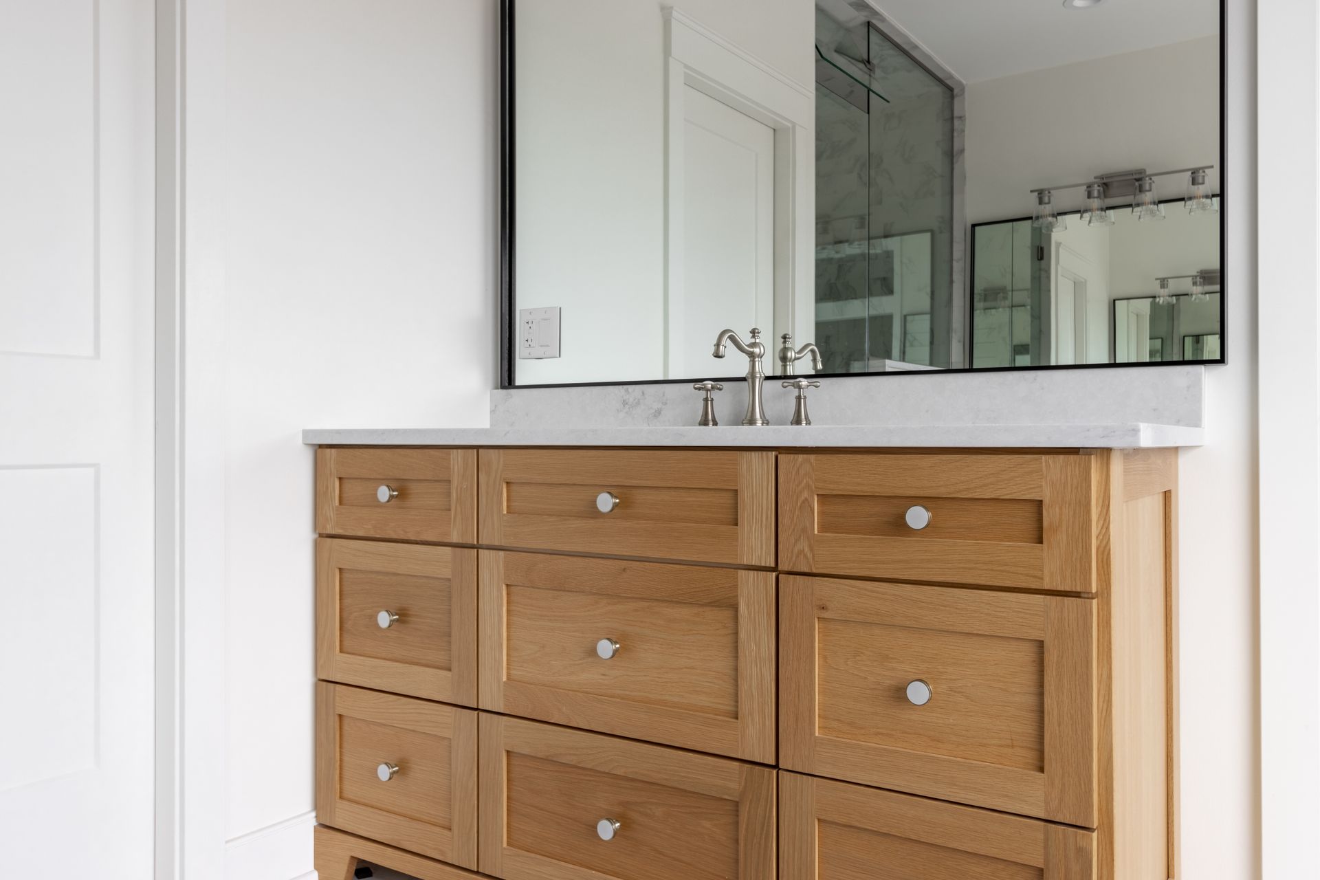 Light oak bathroom vanity with multiple drawers, a large mirror, and a white countertop.