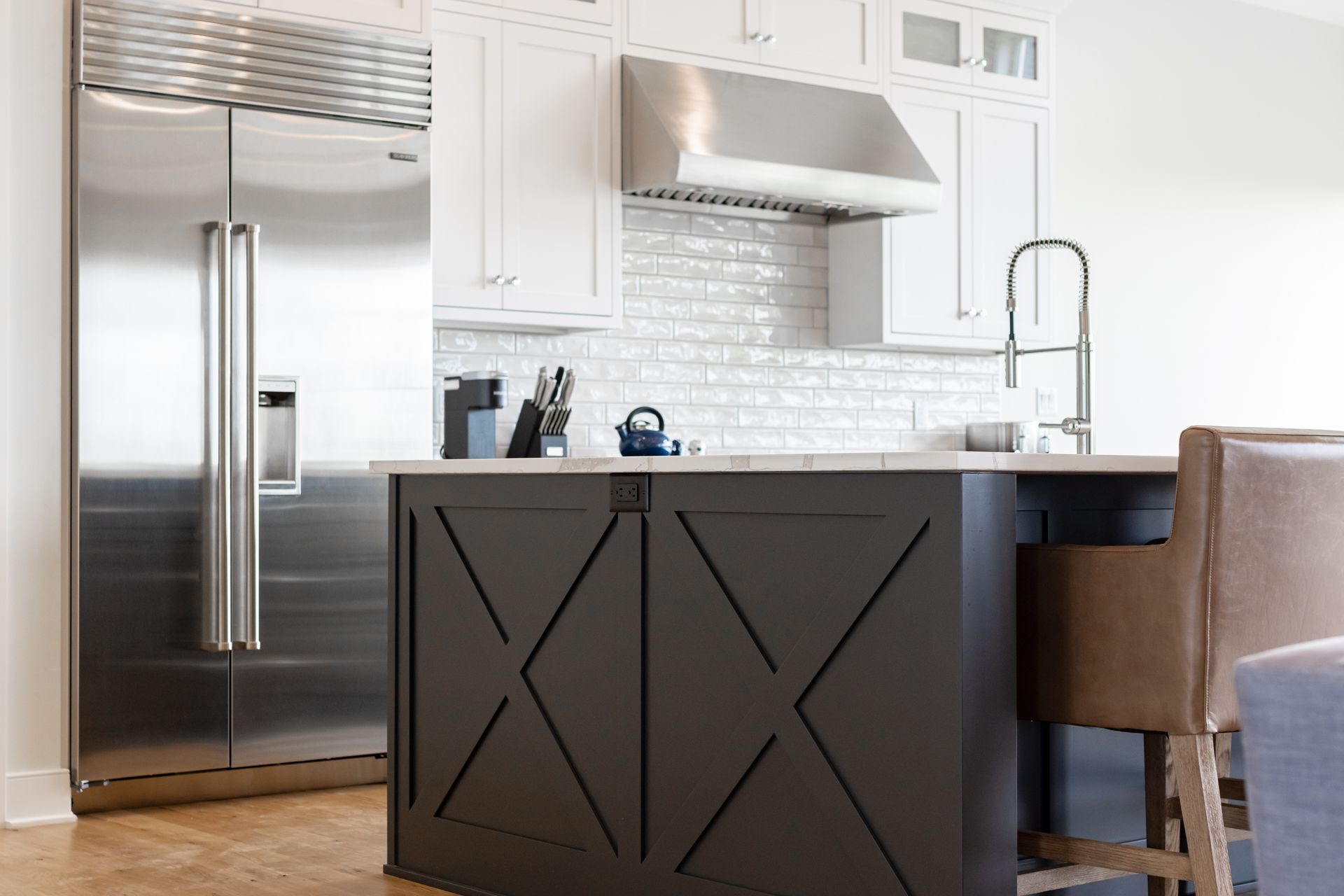 Modern kitchen with a stainless steel refrigerator, white cabinets, and a dark brown island with a wooden design.