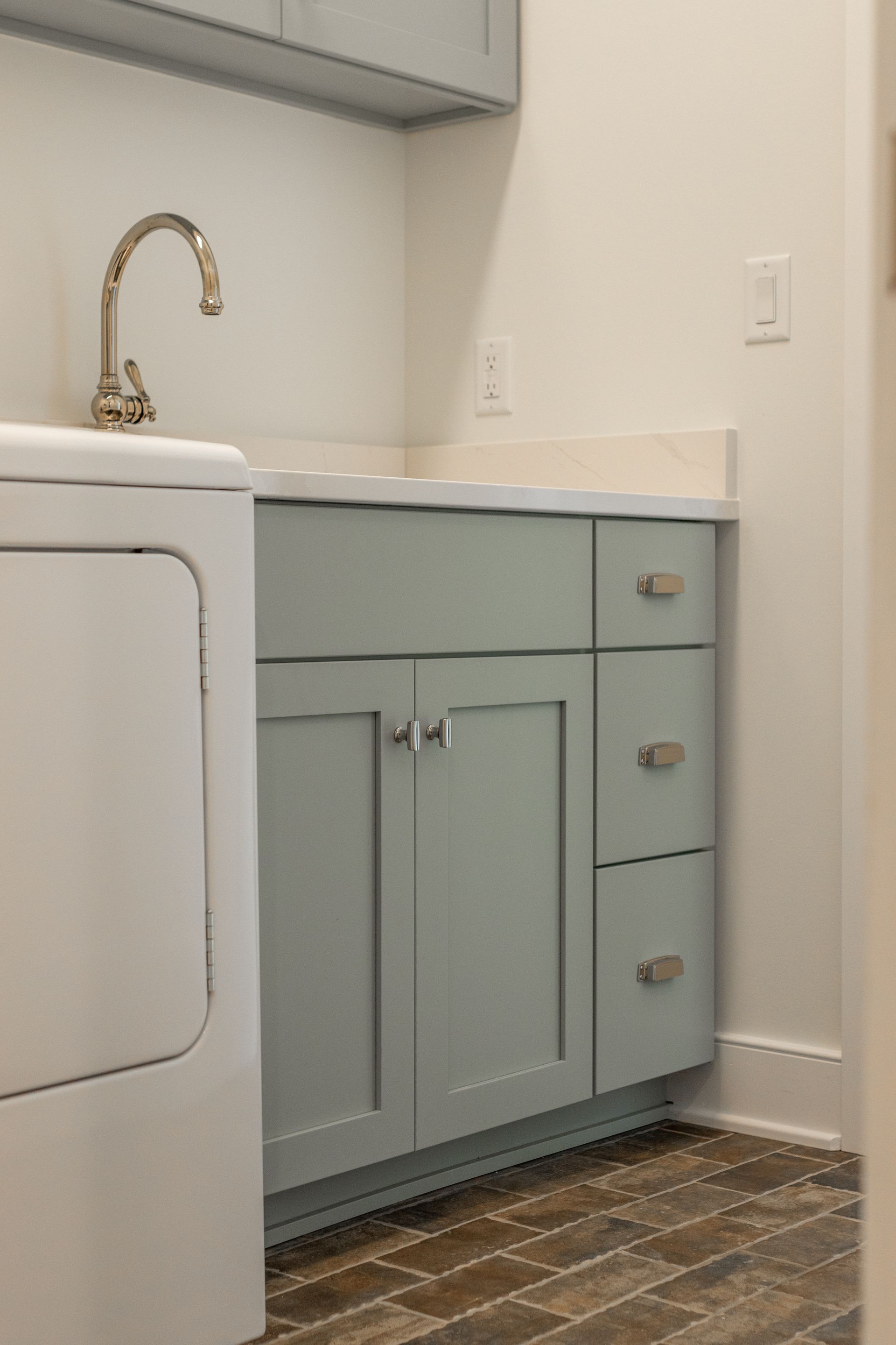 Laundry room with light blue cabinets, white countertop, silver faucet, and wood-look tile floor.