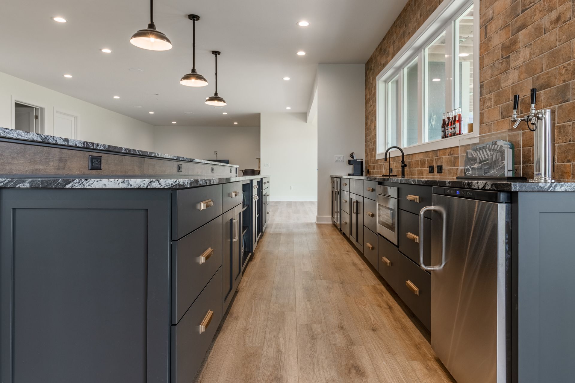 Modern kitchen with grey cabinets, granite countertops, exposed brick wall, and stainless steel appliances.