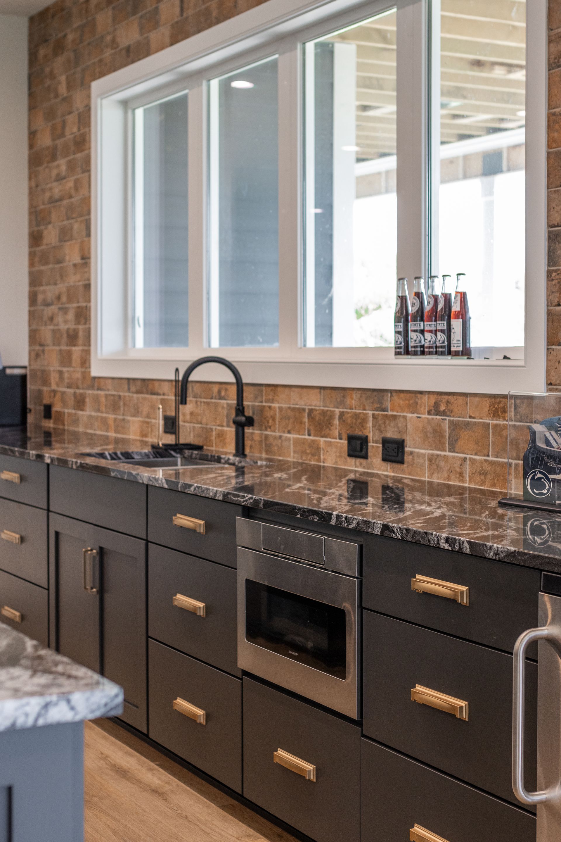 Modern kitchen with dark cabinets, brick backsplash, granite countertop, and stainless steel appliances.