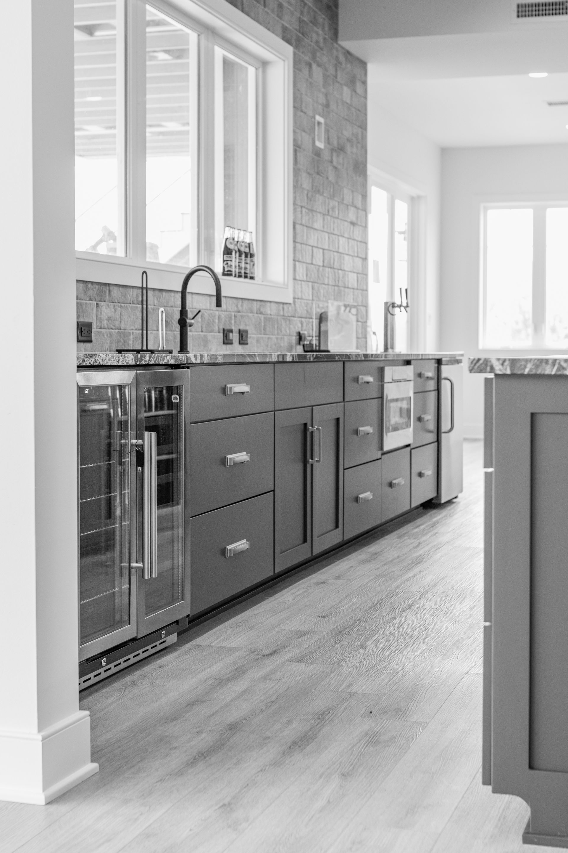 Modern kitchen with island, gray cabinets, stainless steel appliances, and large windows.