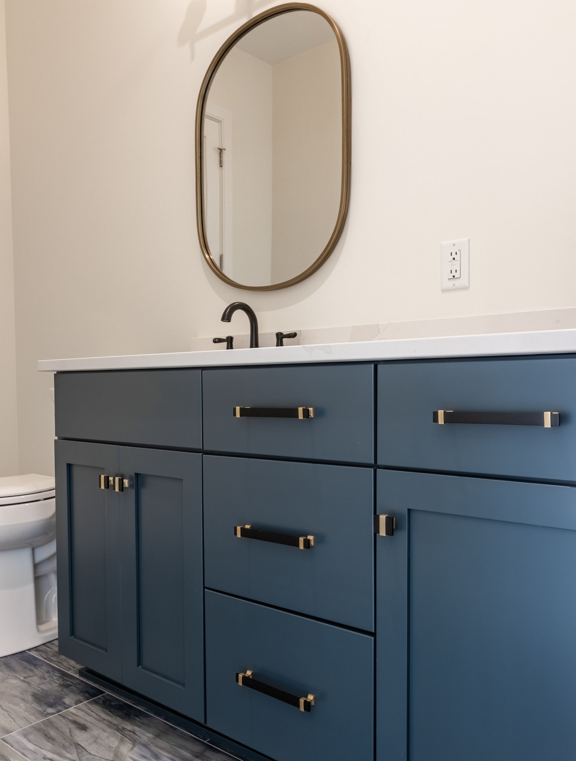 Blue bathroom vanity with gold hardware, white countertop, and oval gold-framed mirror.