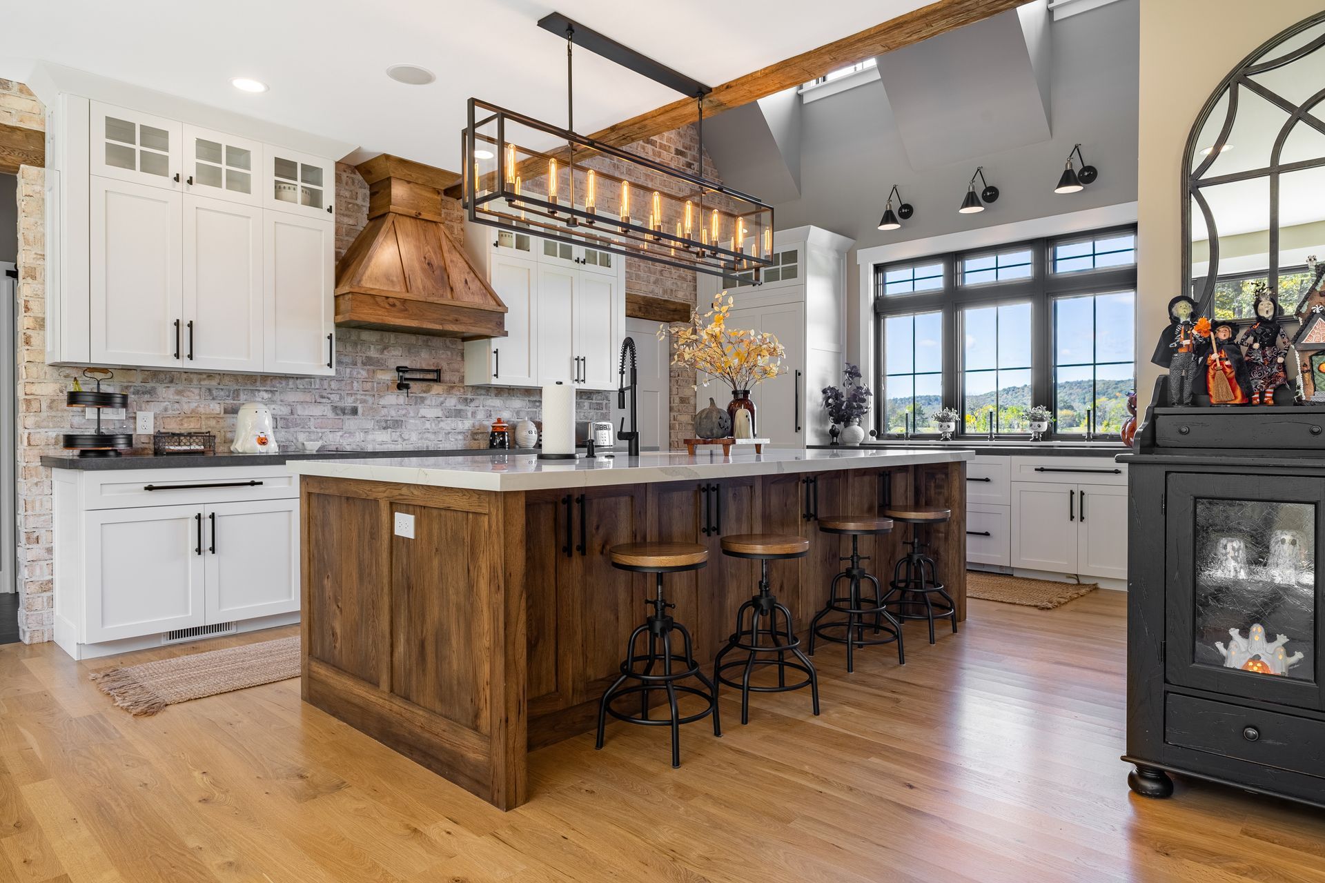 Rustic kitchen with wood island and white cabinets. Overhead lighting, brick backsplash, and large windows.