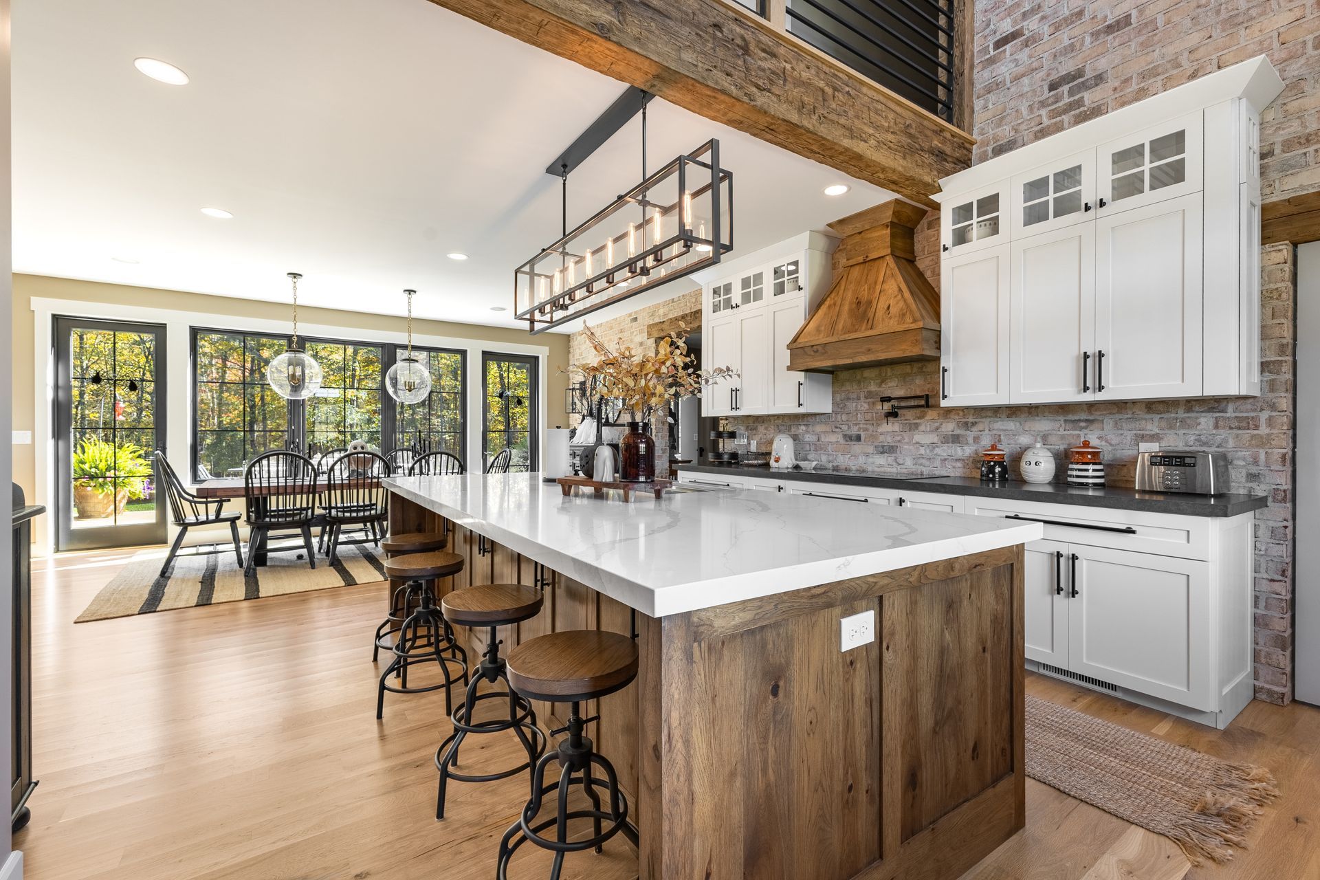 Spacious kitchen with a large island, wood cabinets, and dining area with glass doors overlooking trees.