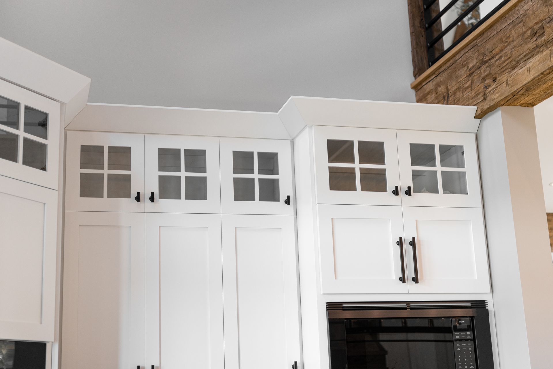 White kitchen cabinets with glass-paned uppers above a microwave, set against a light-colored ceiling.