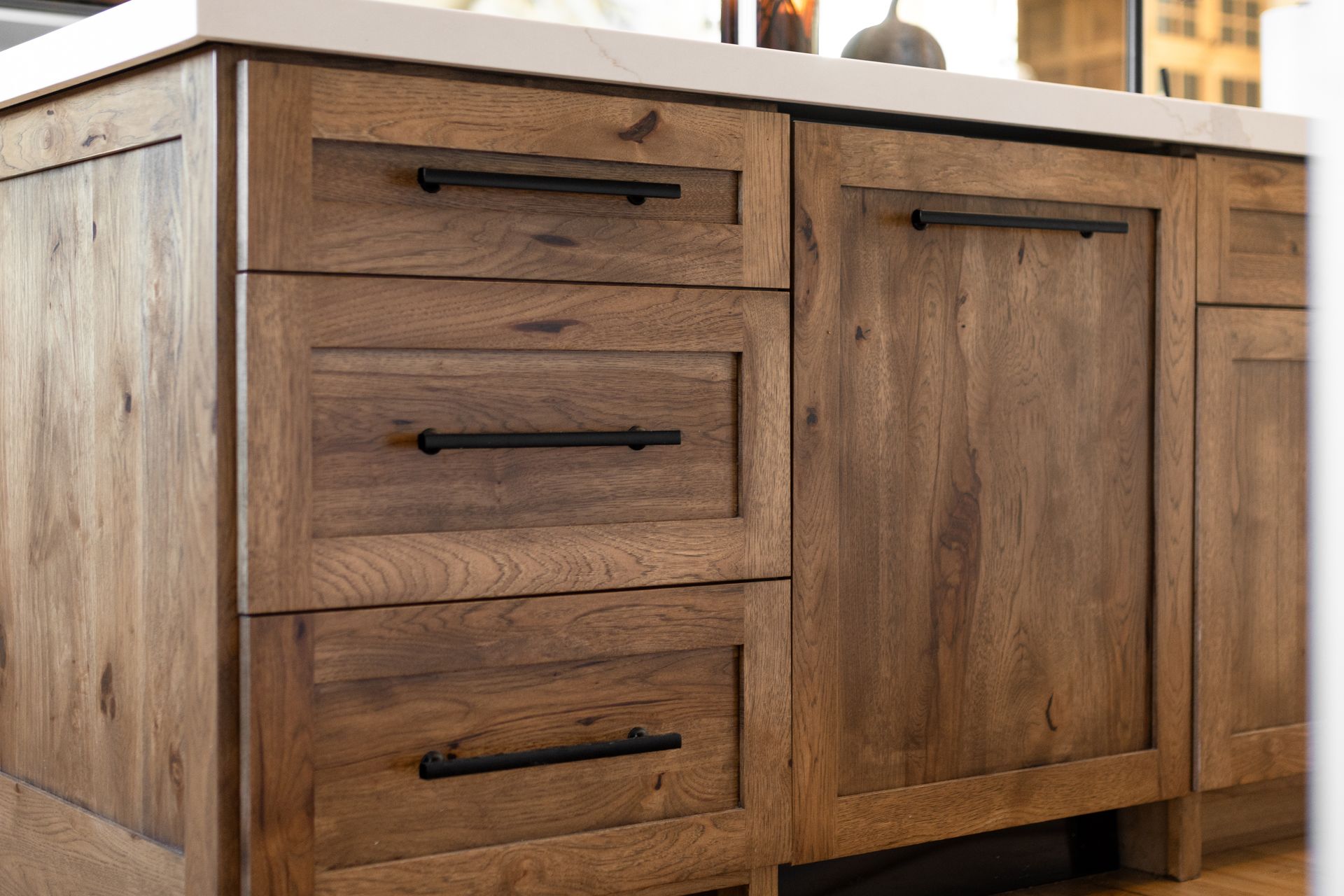 Wooden kitchen cabinets with black handles, set beneath a white countertop.