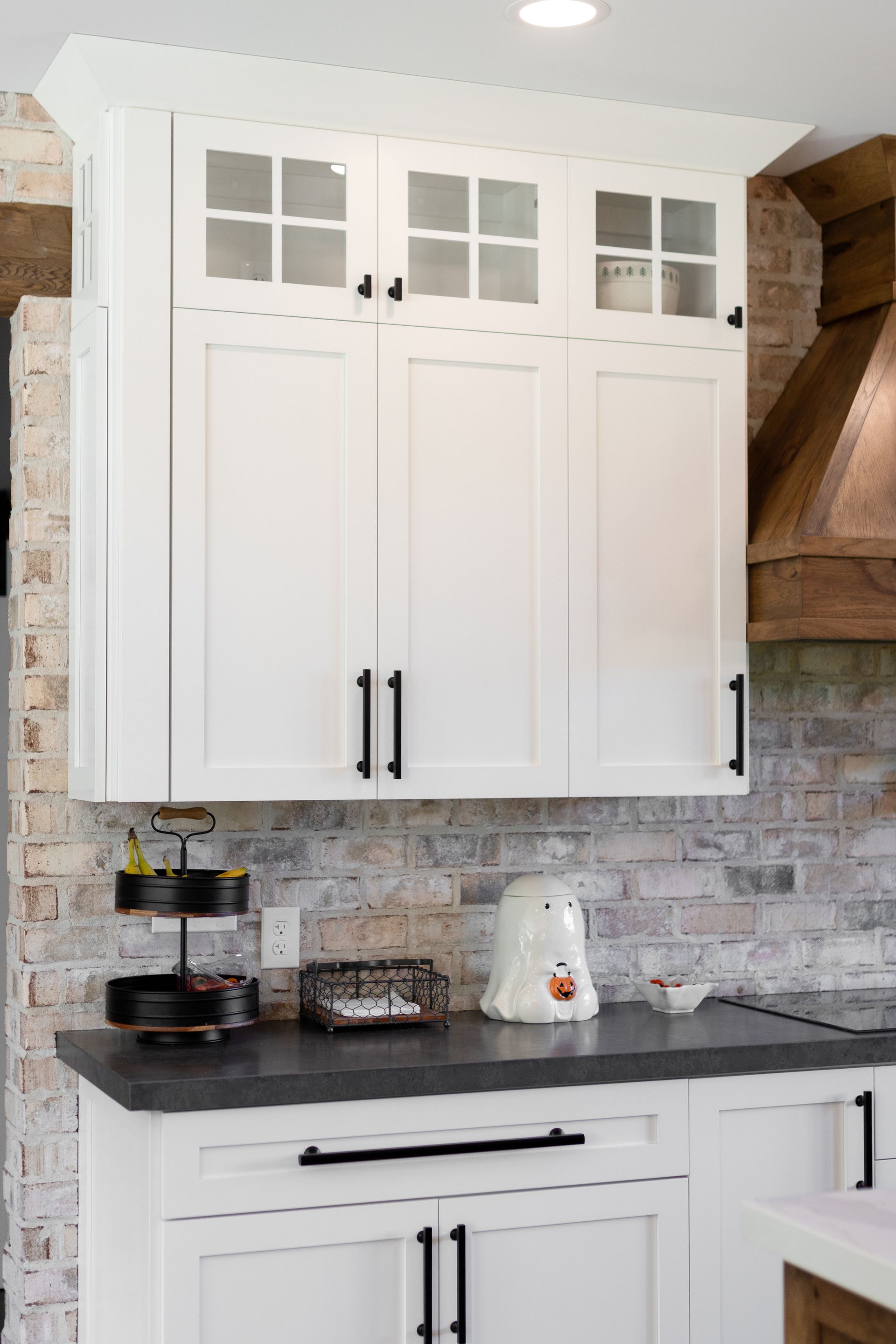 White kitchen cabinets with black hardware against a brick-style backsplash.