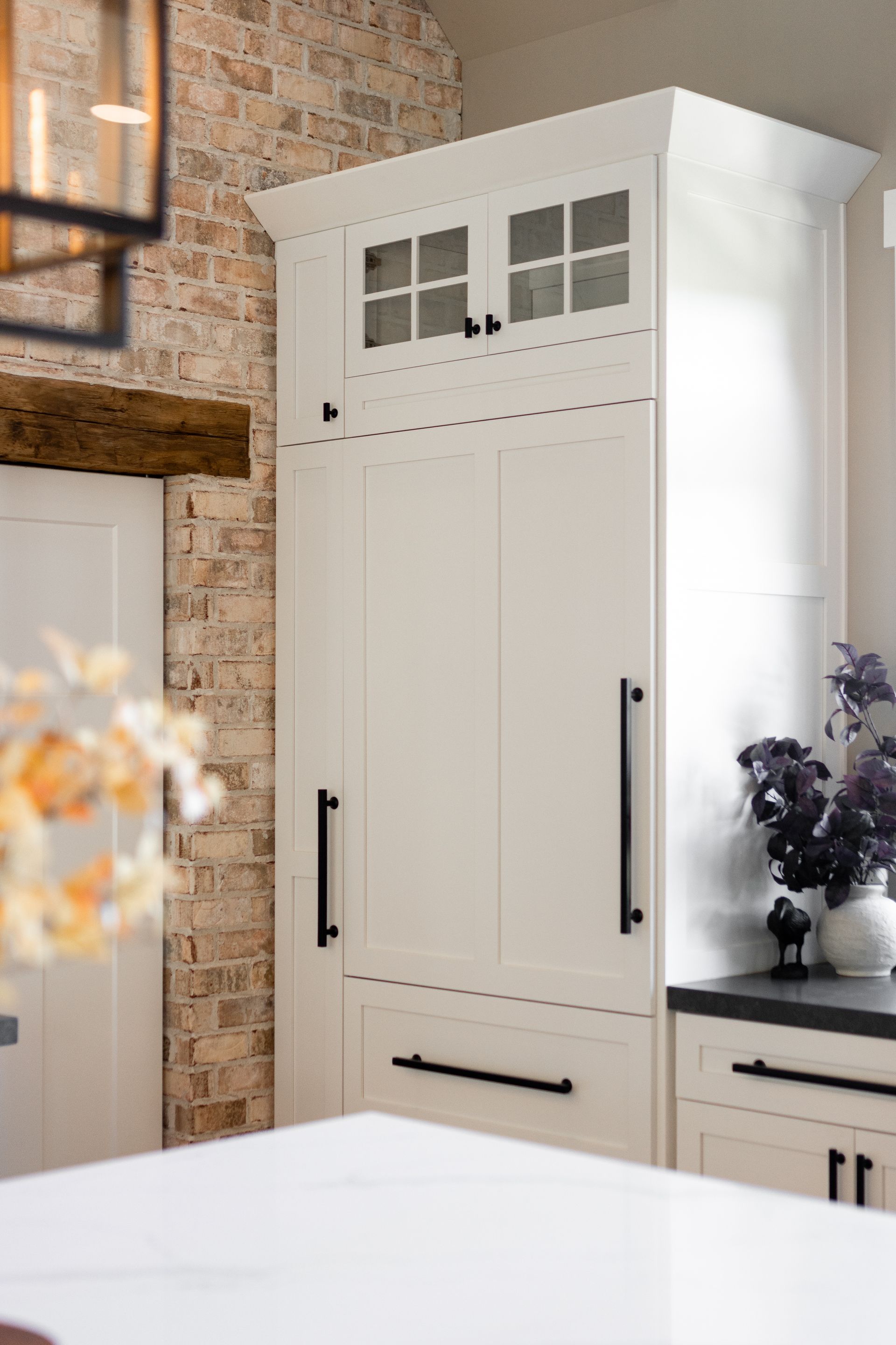 White built-in kitchen cabinet with black hardware, brick wall background.