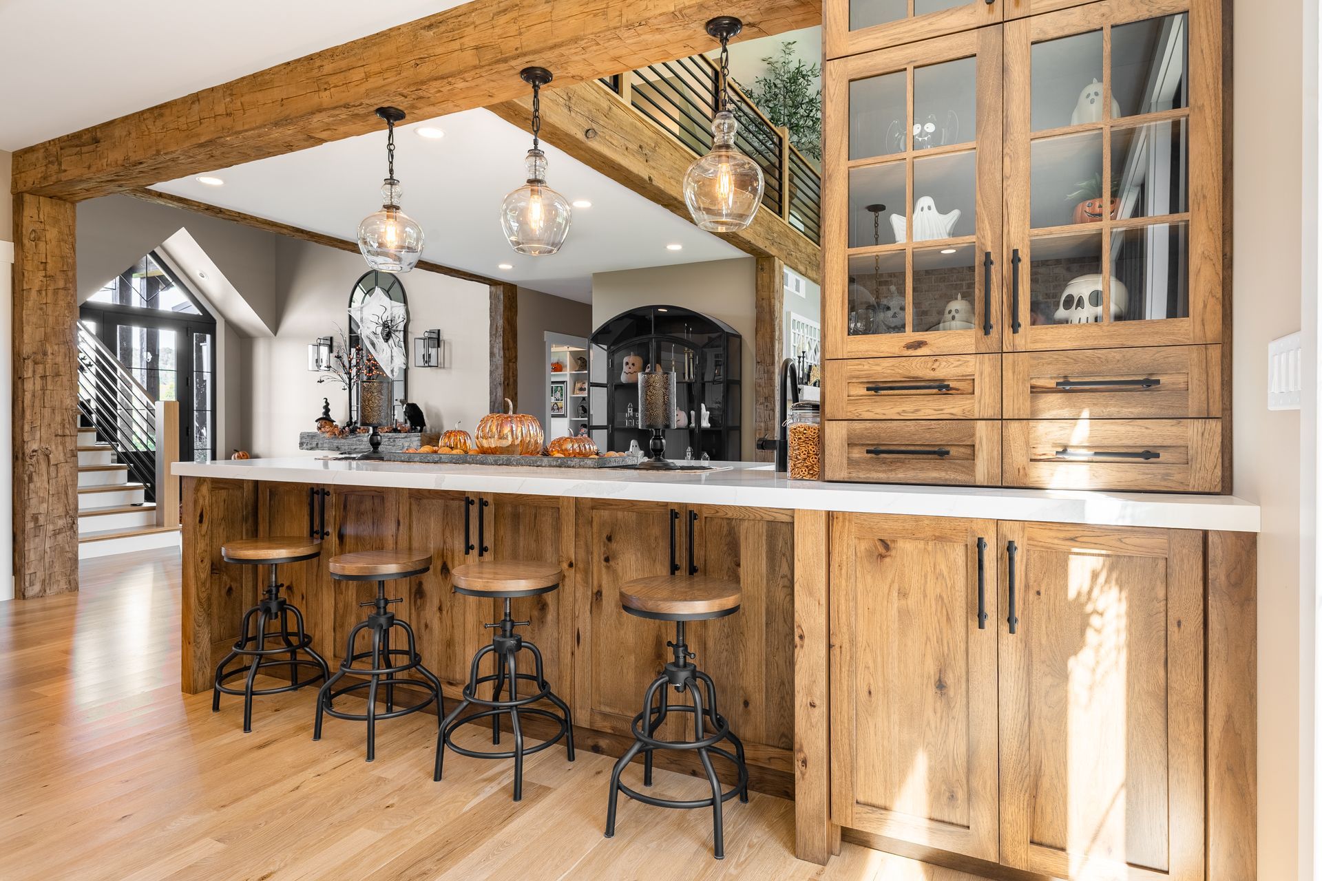Rustic kitchen with wooden cabinets, island, and stools, plus decorative skulls and pumpkins.