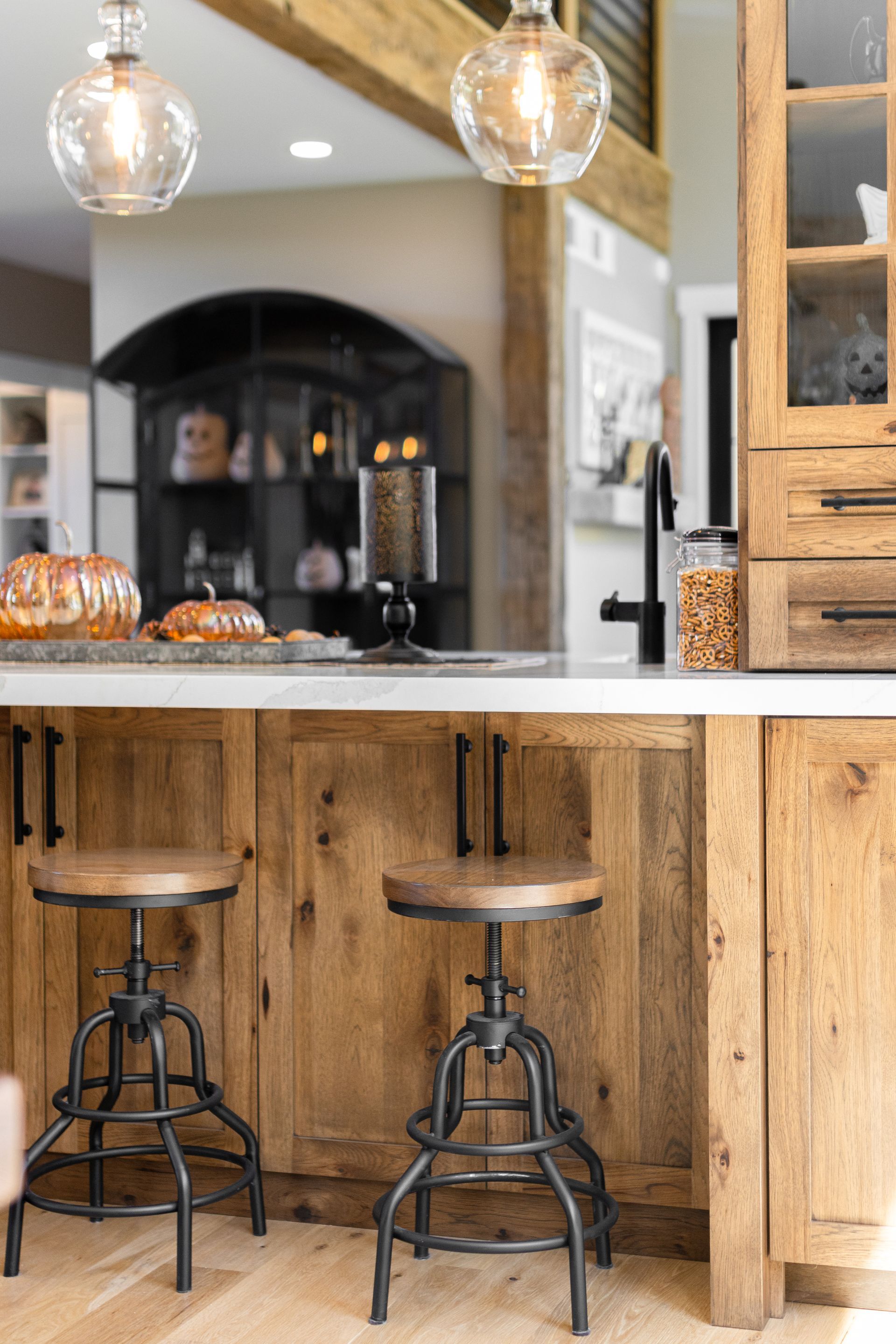 Kitchen island with wooden cabinets, two metal stools, and pendant lights. A baked loaf sits on the countertop.