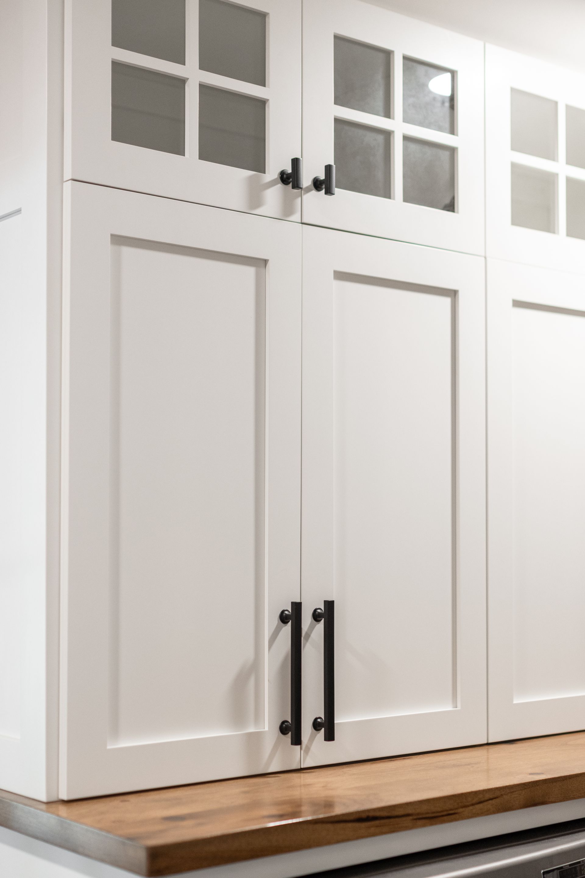 White kitchen cabinets with black handles, set against a wood countertop.