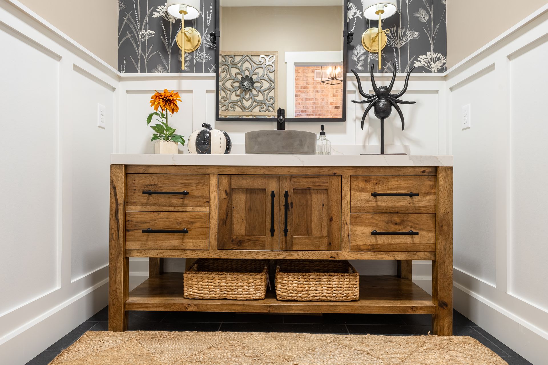 Rustic wooden bathroom vanity with stone countertop, two woven baskets, and a decorative spider.
