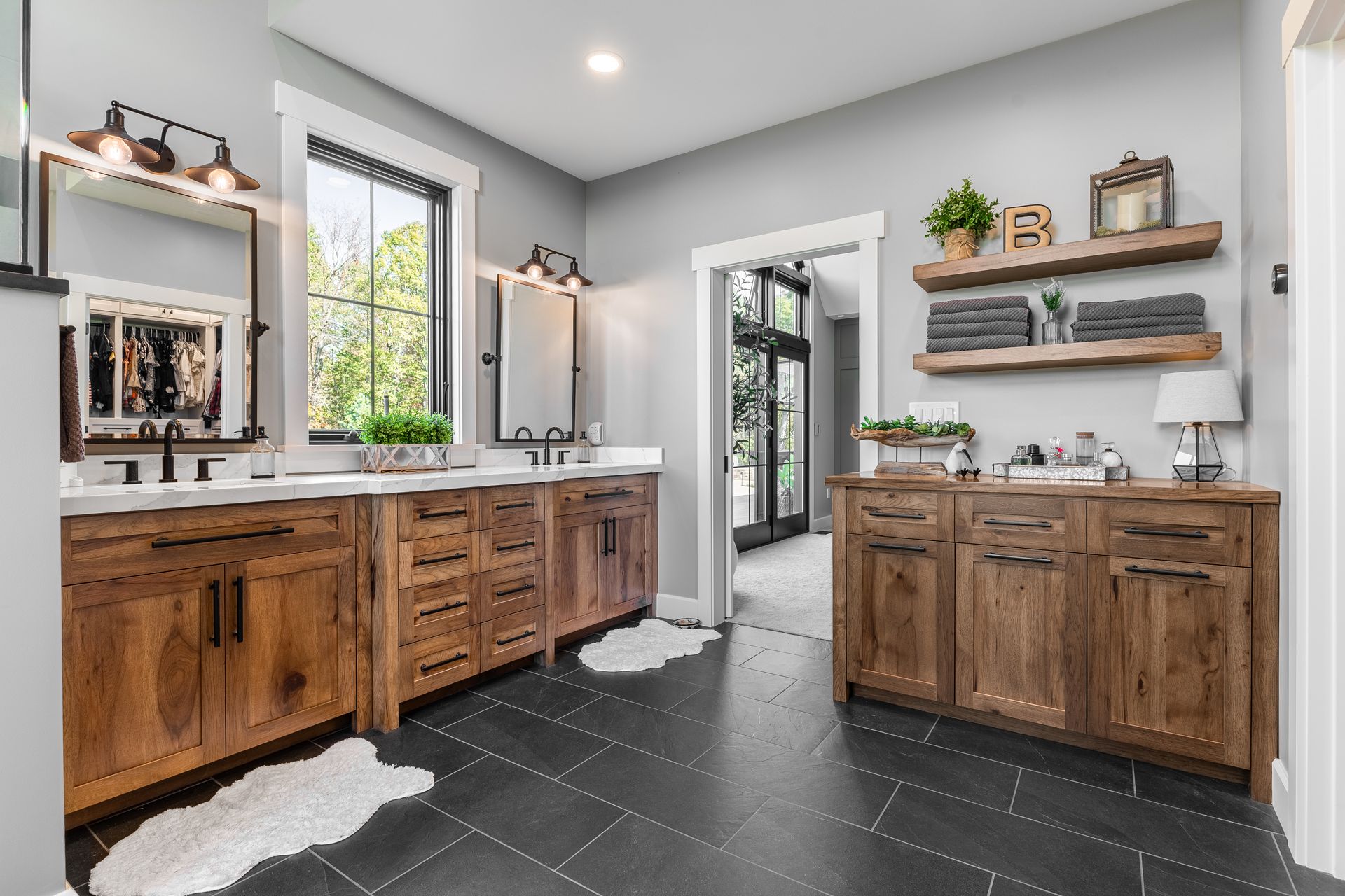Rustic-style bathroom with wooden vanities, gray walls, black tile floor, and an open doorway.