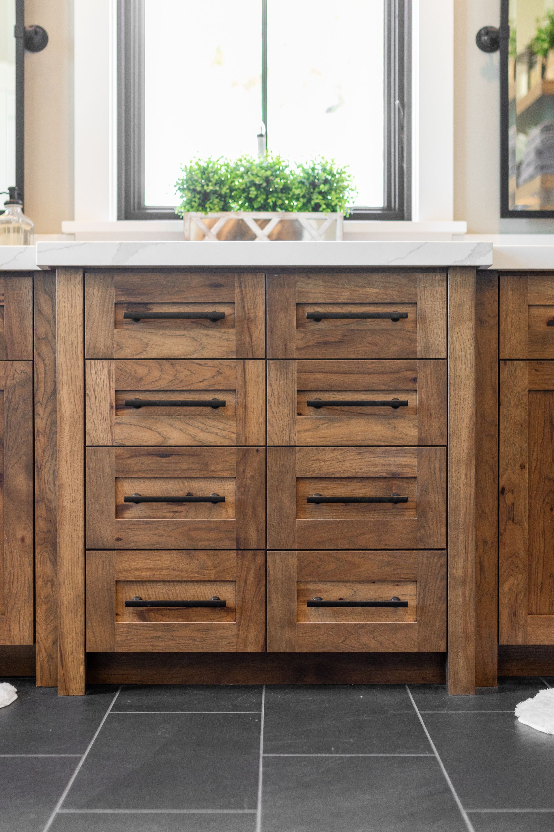 Wooden bathroom cabinet with six drawers, black handles, and dark tile floor.