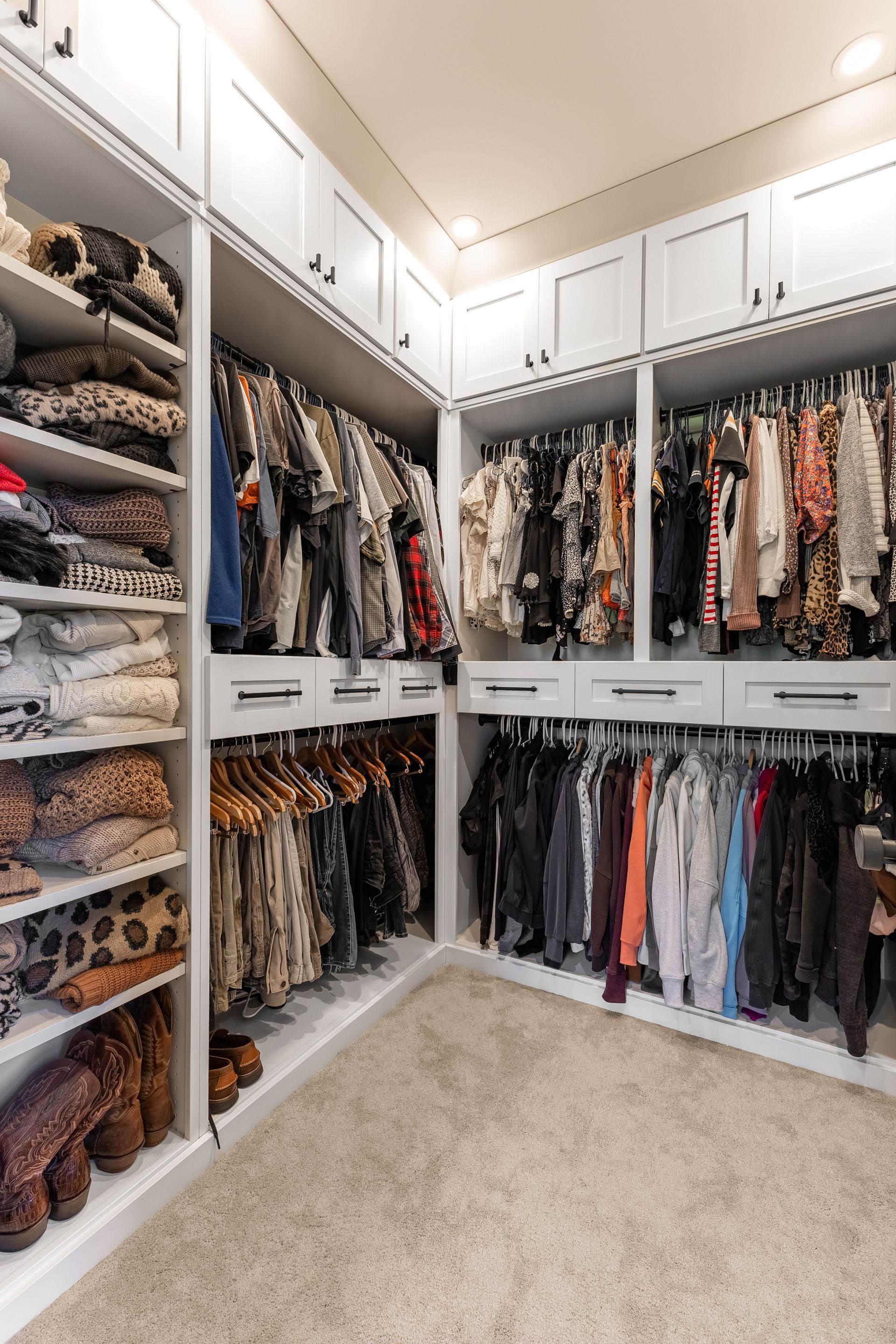 Walk-in closet with white cabinets, hanging clothes, and shelves with folded garments.