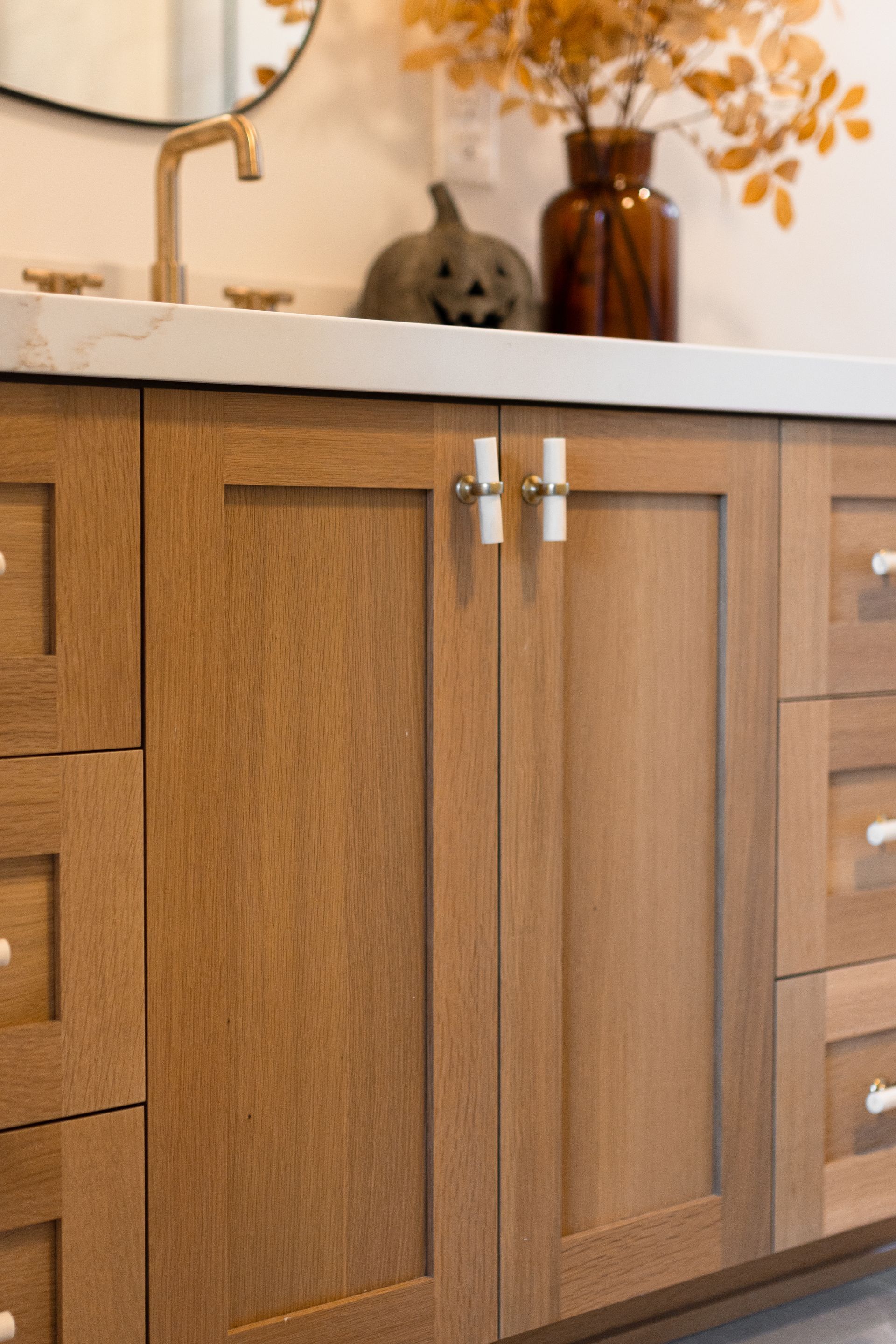 Wooden bathroom vanity with white countertop and gold fixtures; fall decor.