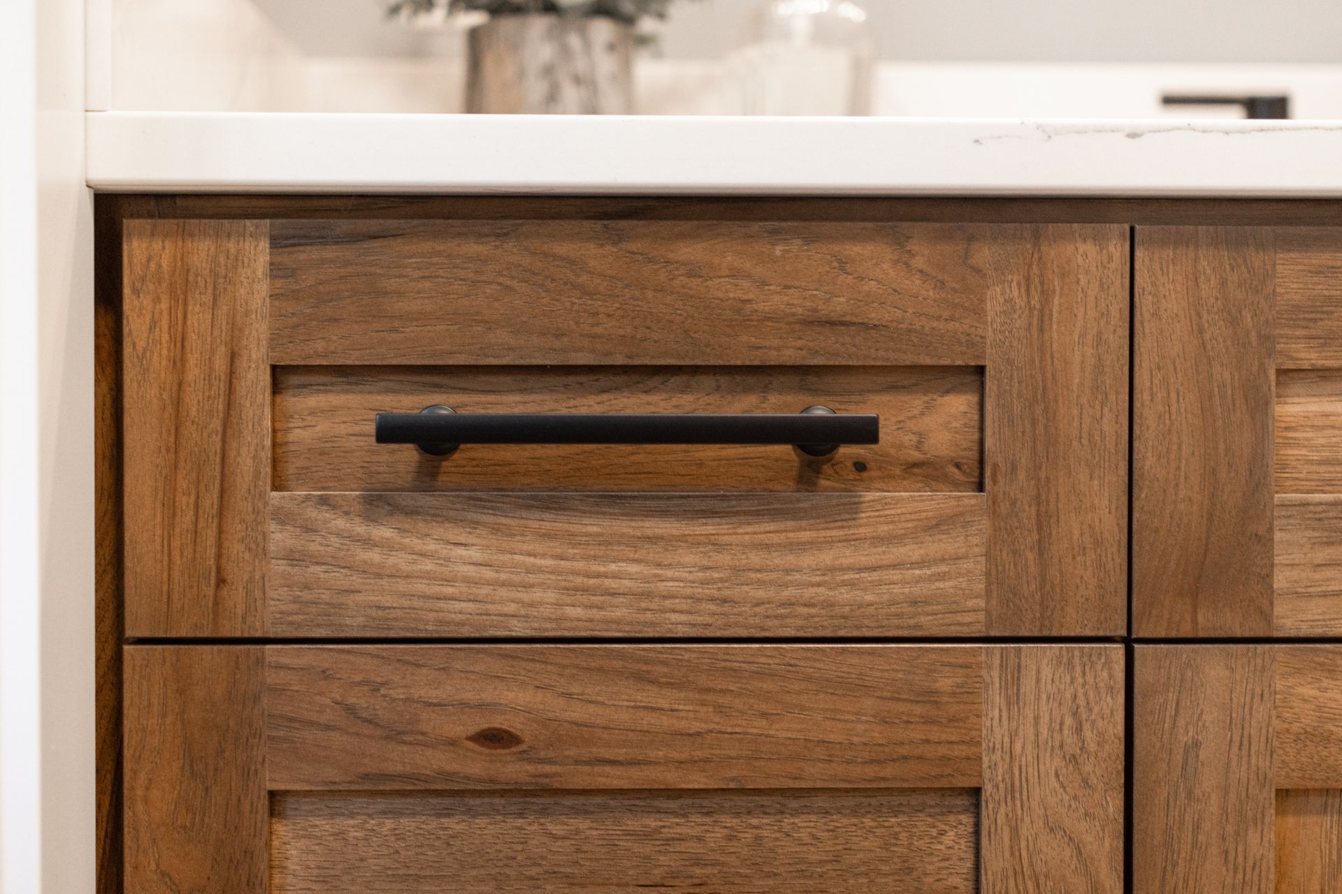 Wooden kitchen cabinet drawer with black handle, white countertop in the background.